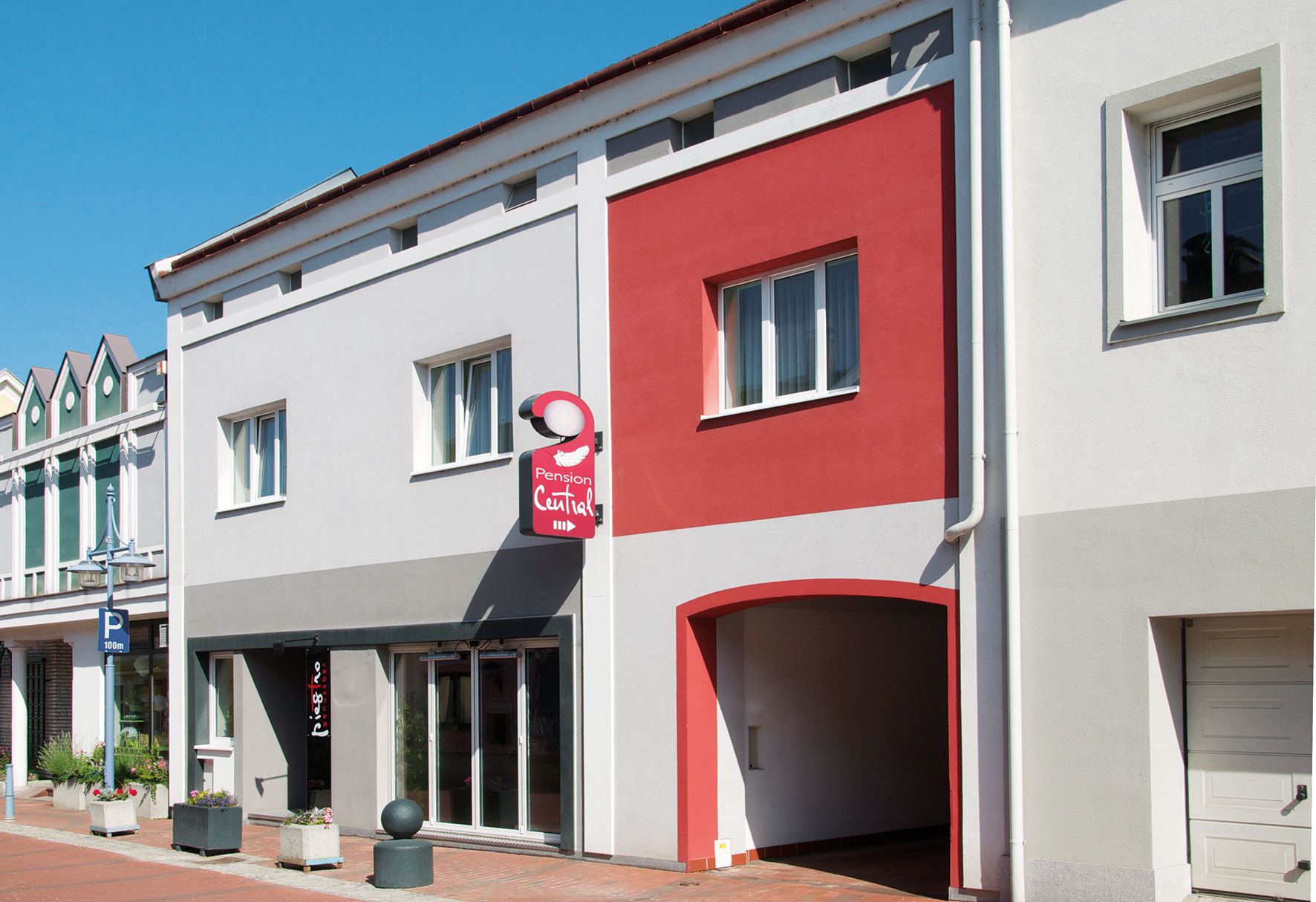 Fasáda penzionu Central s šedými a červenými stěnami, nápisem a okny.