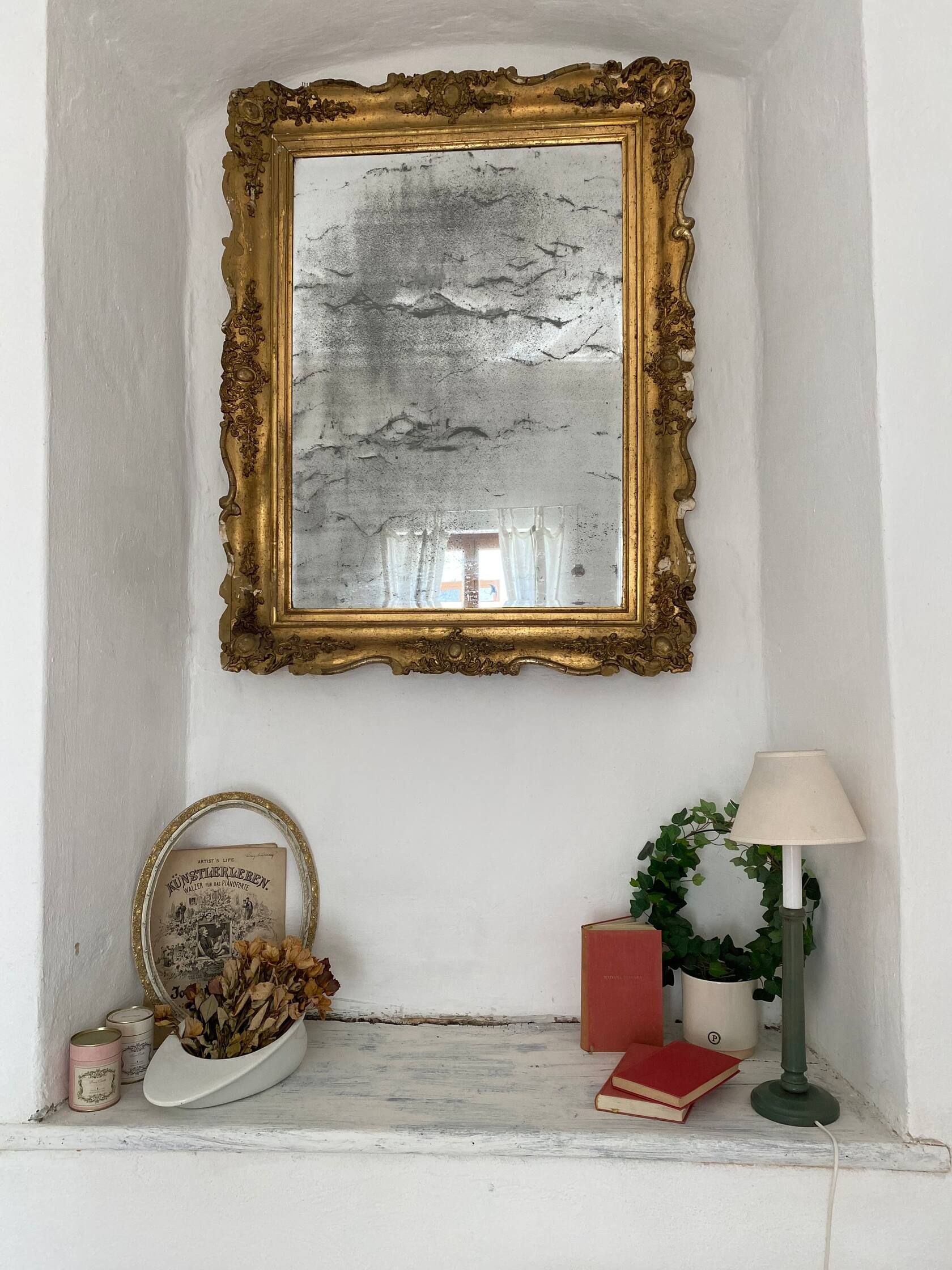 Starožitné zrcadlo se zlatým dekorem nad okenním parapetem s dekorem.