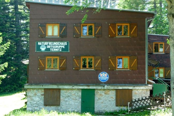Třípatrová budova s dřevěnými okenicemi a nápisy Naturfreunde Ternitz.