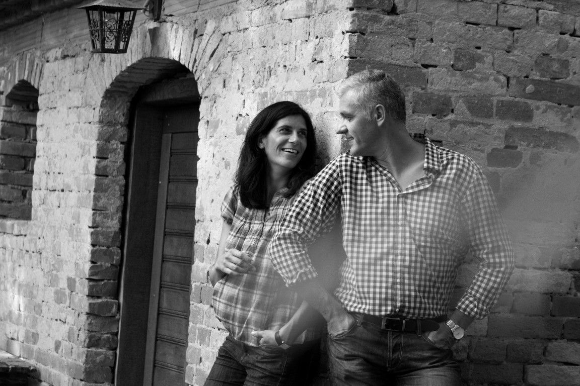 Muž a žena se s úsměvem opírají o cihlovou zeď.