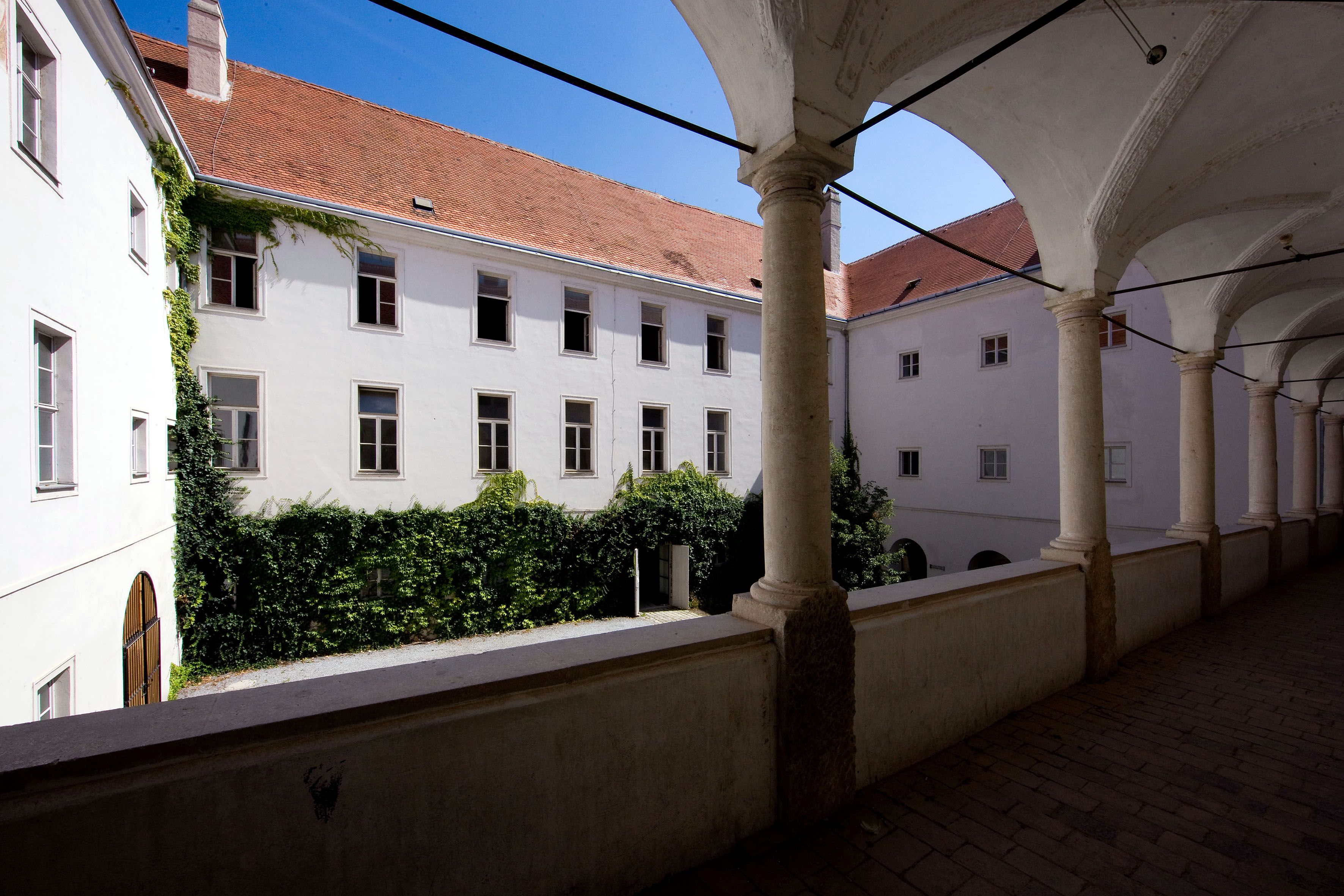Vnitřní nádvoří historické budovy s podloubím a zdmi porostlými břečťanem.