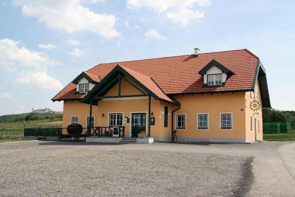 Žlutá budova s červenou střechou a zelenými akcenty, obklopená venkovskou krajinou.