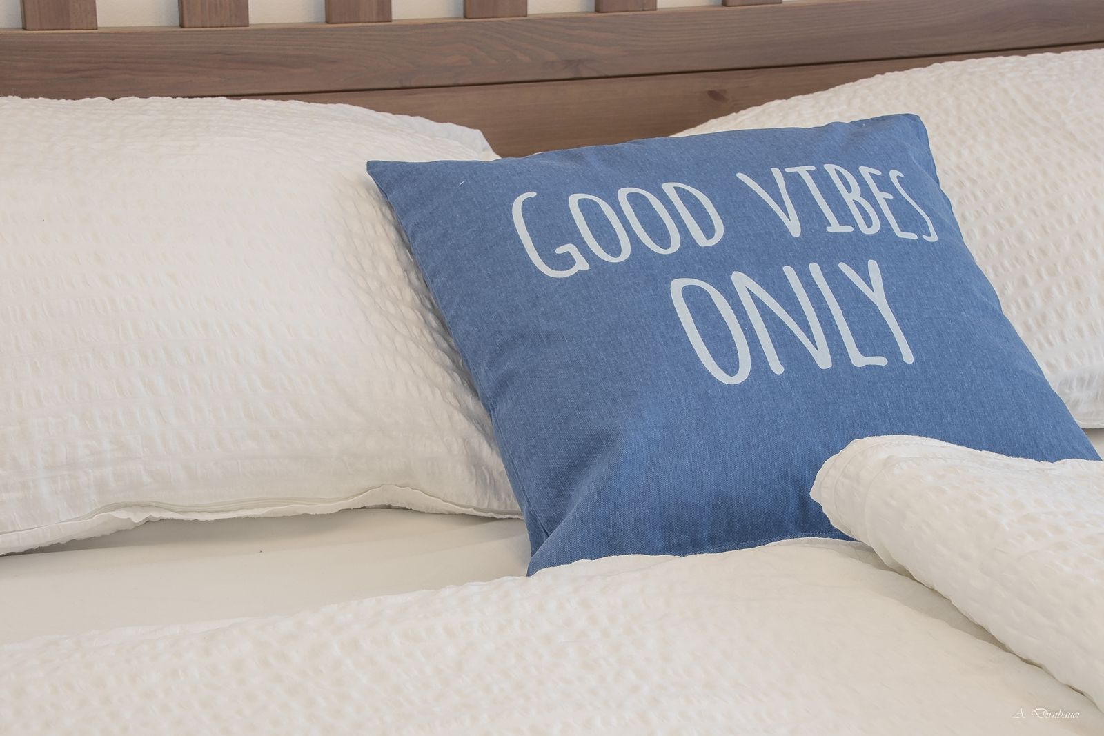 Postel s modrým polštářem s nápisem "Good Vibes Only".