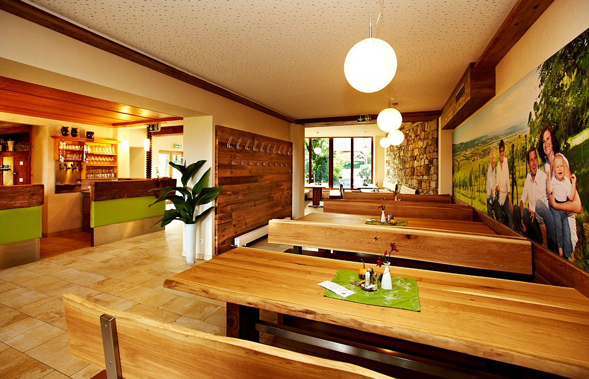 Pohled do interiéru útulné restaurace s dřevěnými stoly a lavicemi, zdobené rostlinami a velkou nástěnnou malbou.