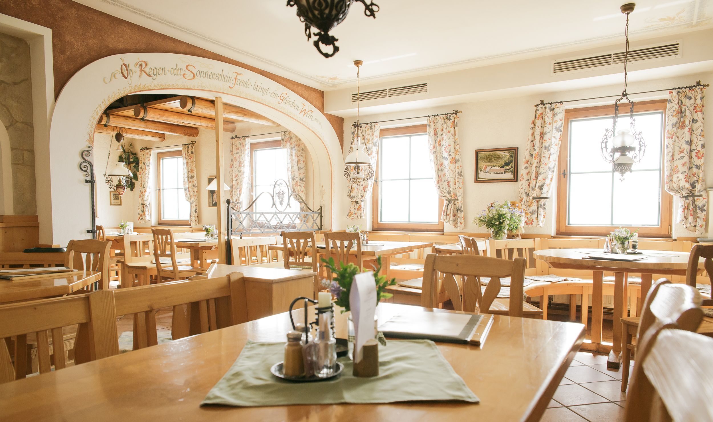Pohled do interiéru útulné restaurace s dřevěným nábytkem a květinovými závěsy.