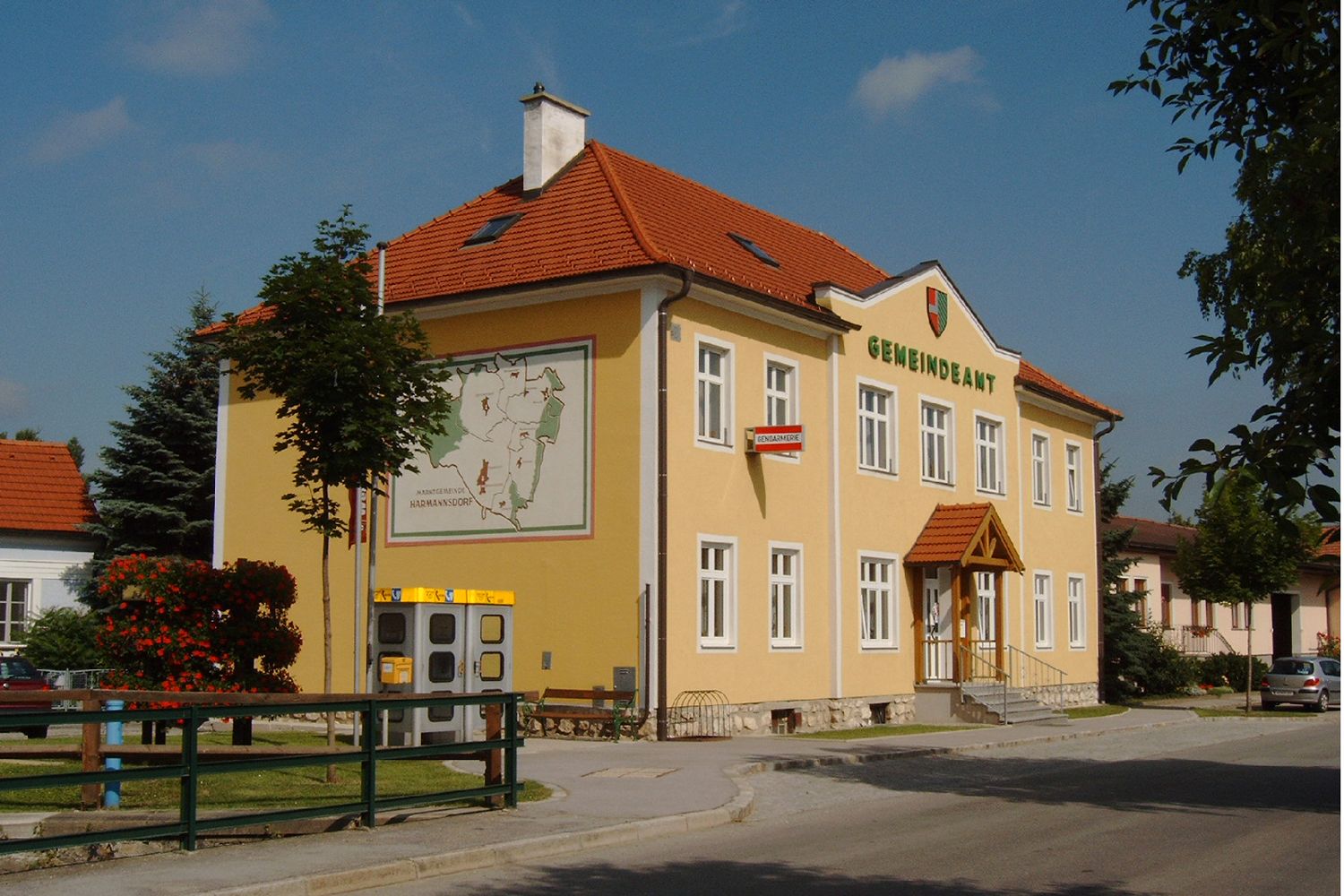 Žlutá budova s nápisem "Gemeindeamt", erbem a Mapou na zdi.