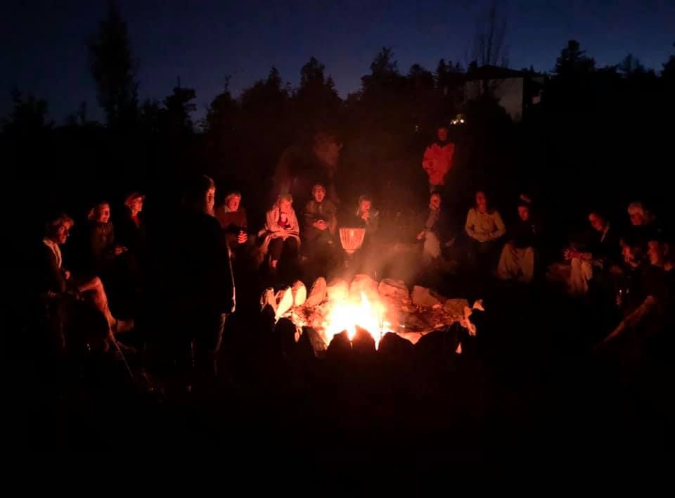 Lidé sedí v noci v kruhu kolem táboráku.