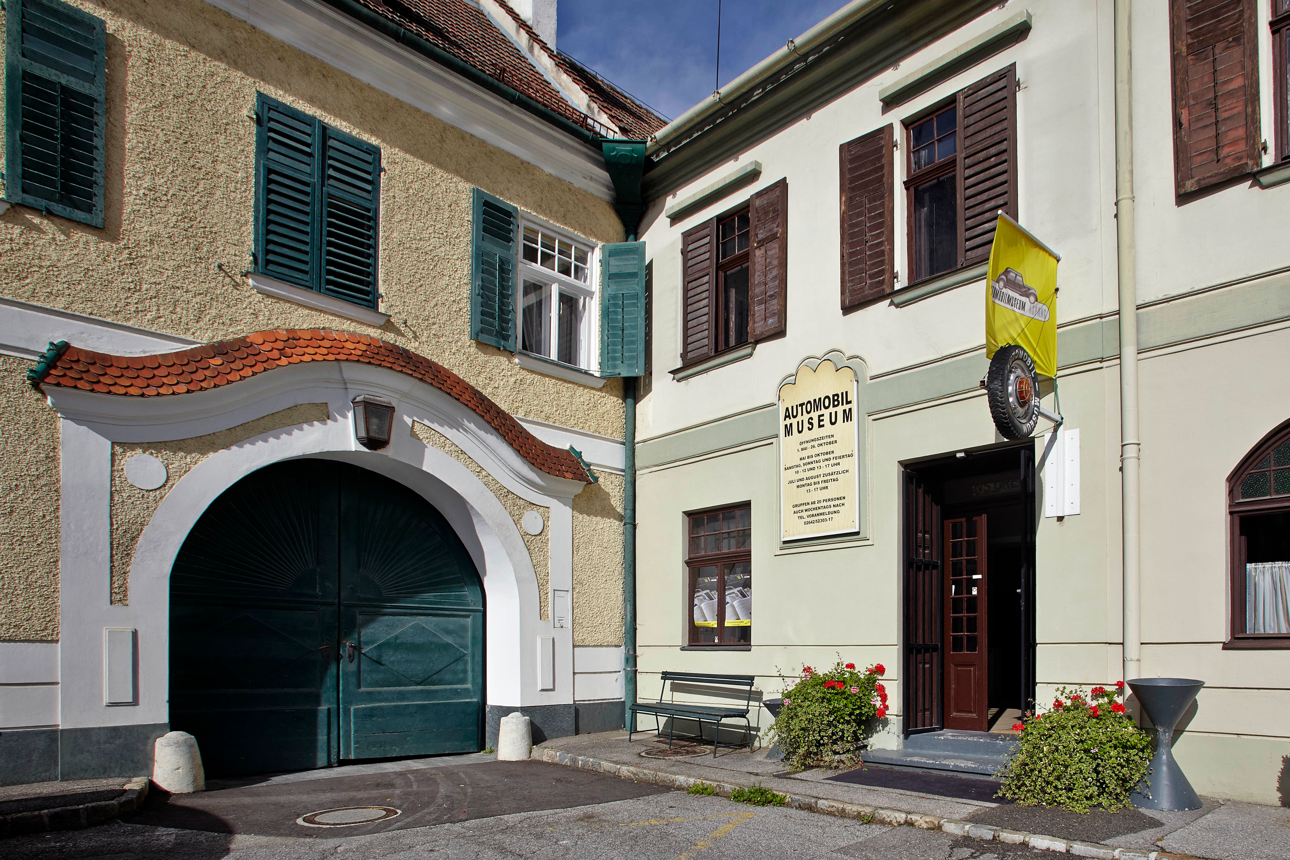 Vchod do automobilového muzea Aspang Market se žlutou vlajkou a květinami.