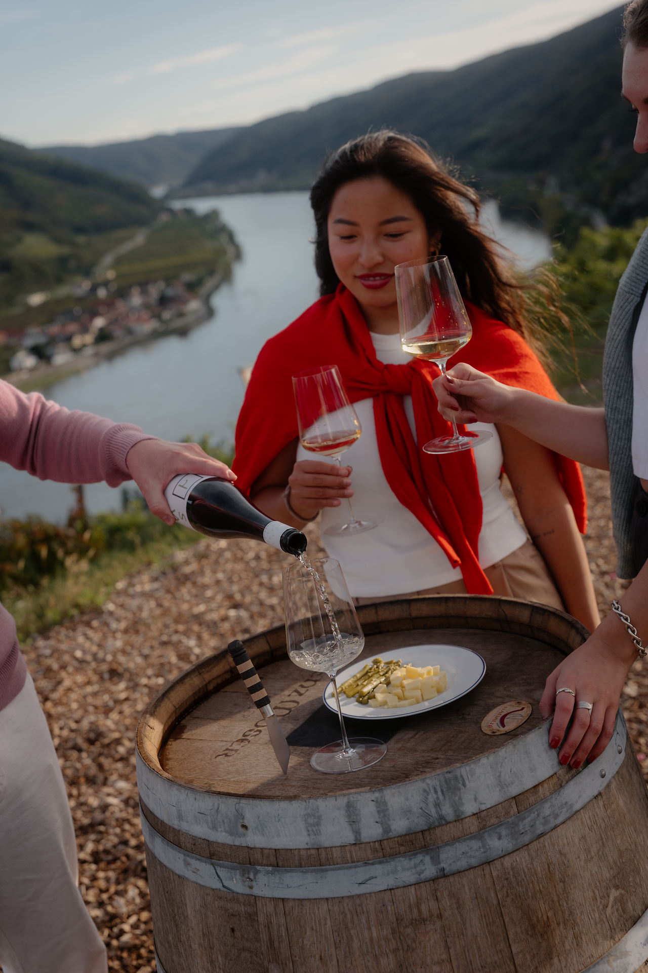 Drei Personen genießen ein Glas Wein in der Wachau, im Hintergrund sieht man die Donau fließen.