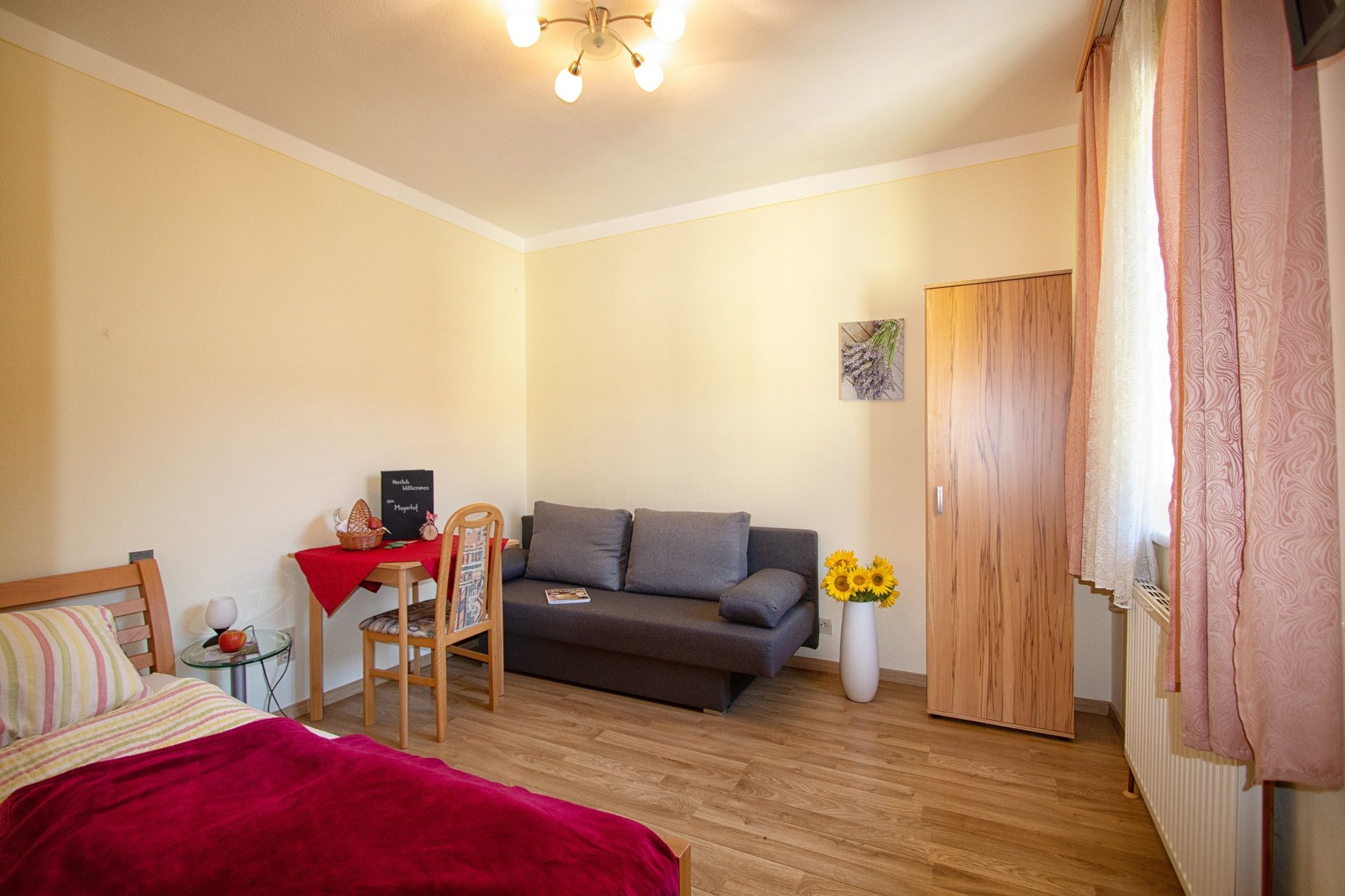 Útulný pokoj s postelí, pohovkou, stolem a šatní skříní, zdobený slunečnicemi a obrazem na stěně.