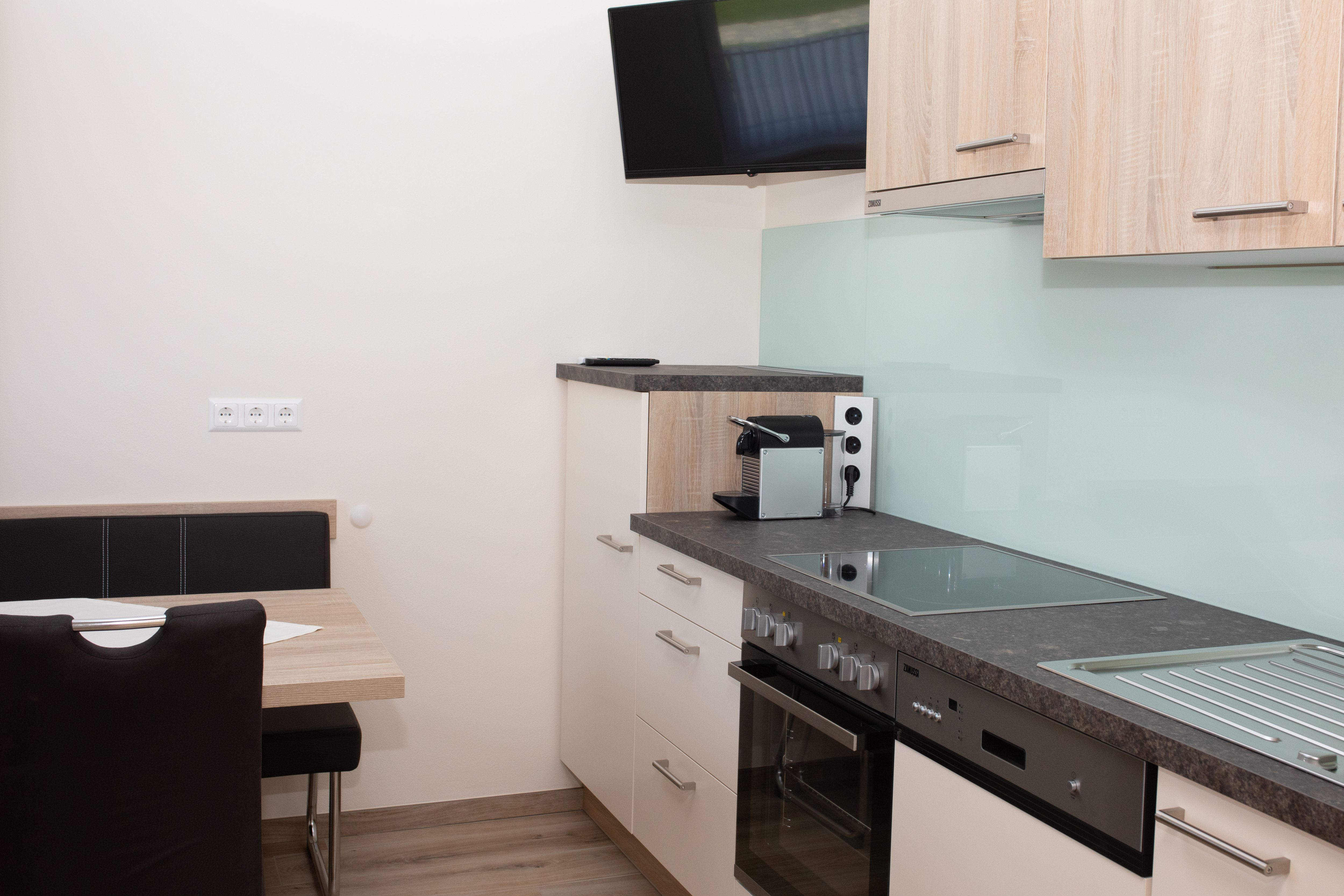 Moderní kuchyně se sporákem, dřezem, kávovarem a nástěnnou TV.