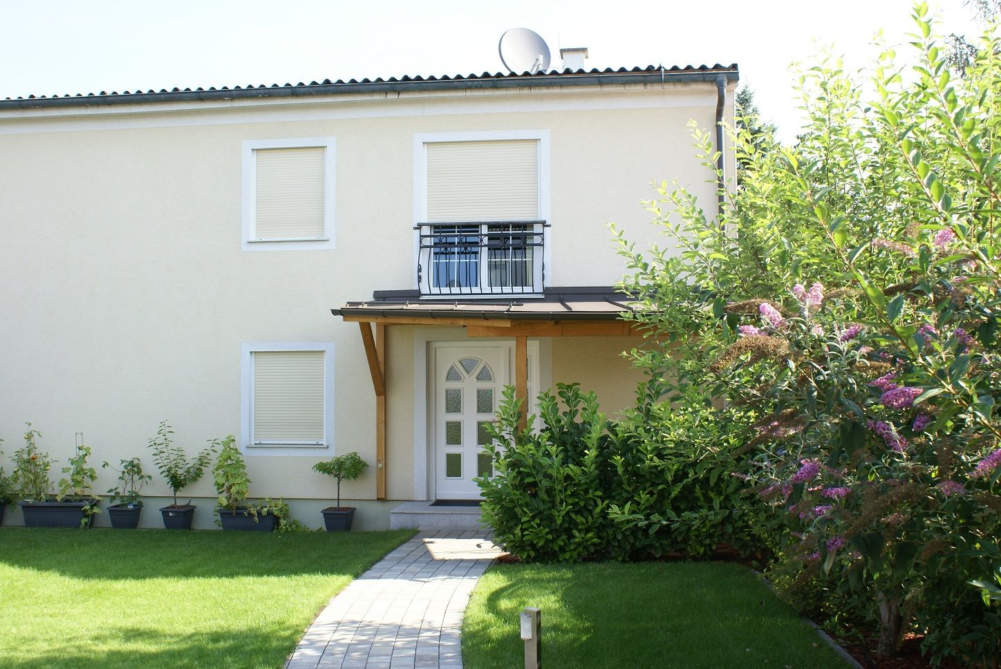 Pohled zvenčí na dvoupodlažní dům se zahradou a rostlinami.