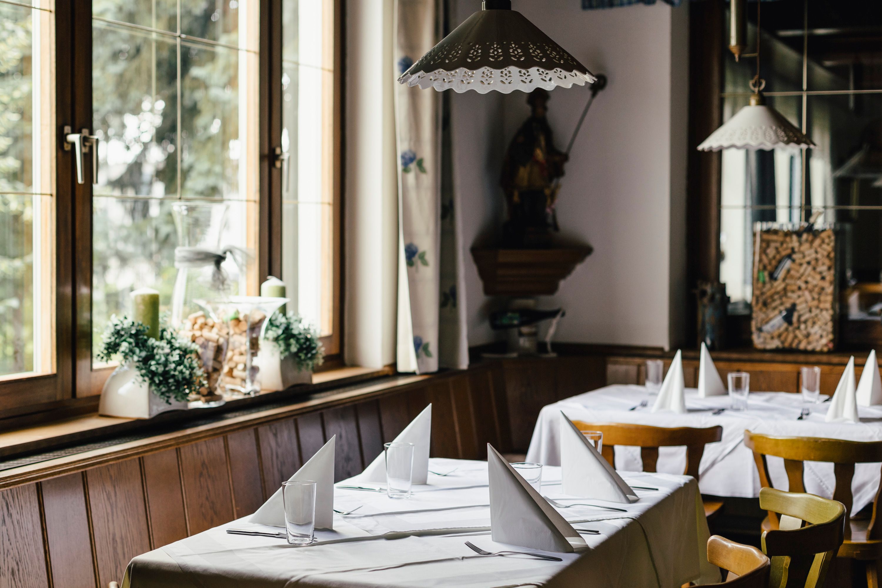 Pohled do interiéru útulné restaurace s prostřenými stoly a dřevěnými židlemi.