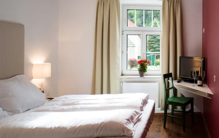 Manželská postel s oknem a rohovým stolem s TV