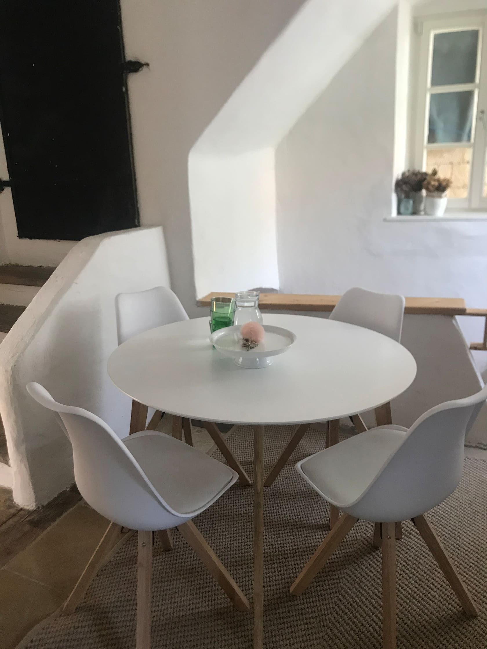 Moderní posezení s kulatým stolem a čtyřmi bílými židlemi ve světlé místnosti.