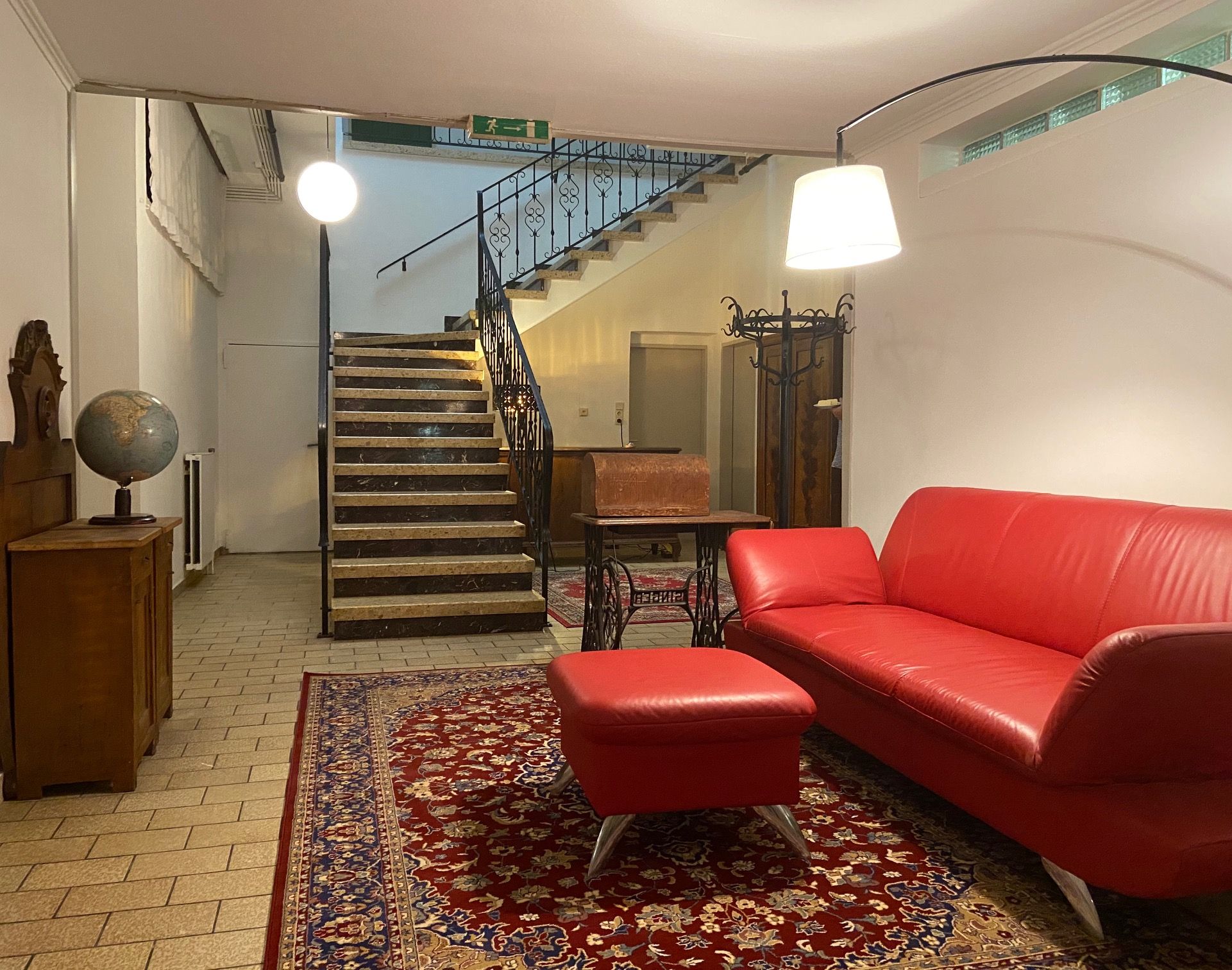 Foyer s červenou pohovkou, kobercem, glóbusem a schodištěm.