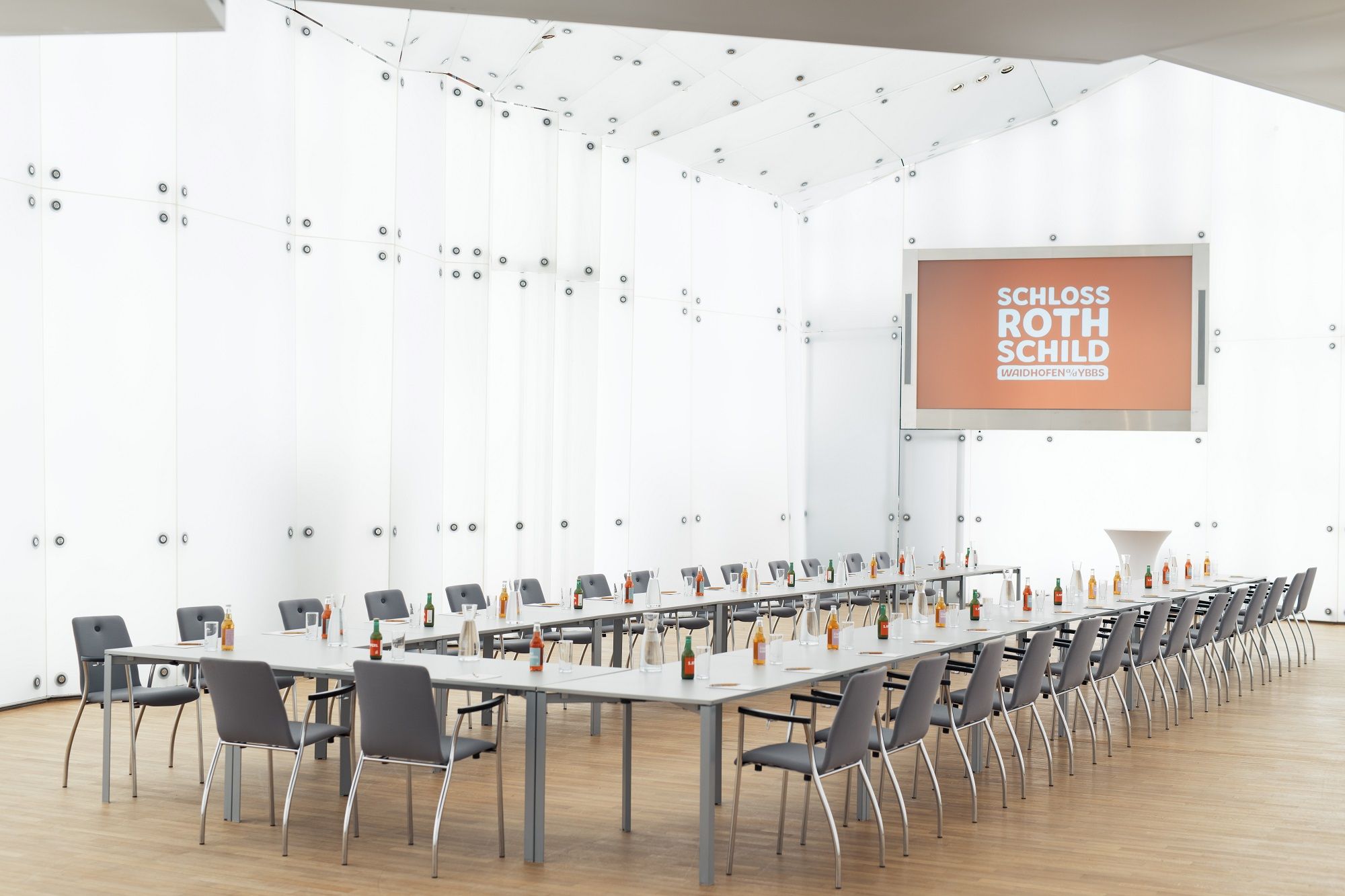 Moderní konferenční místnost na zámku Rothschild s dlouhými stoly, židlemi a nápoji.
