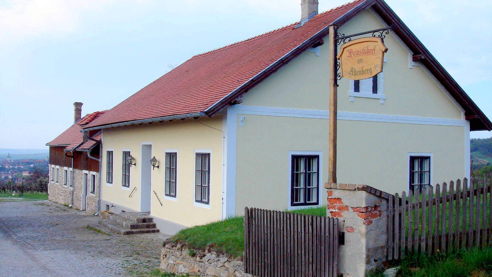 Vinařský dům se žlutou fasádou a červenou střechou ve venkovském prostředí.