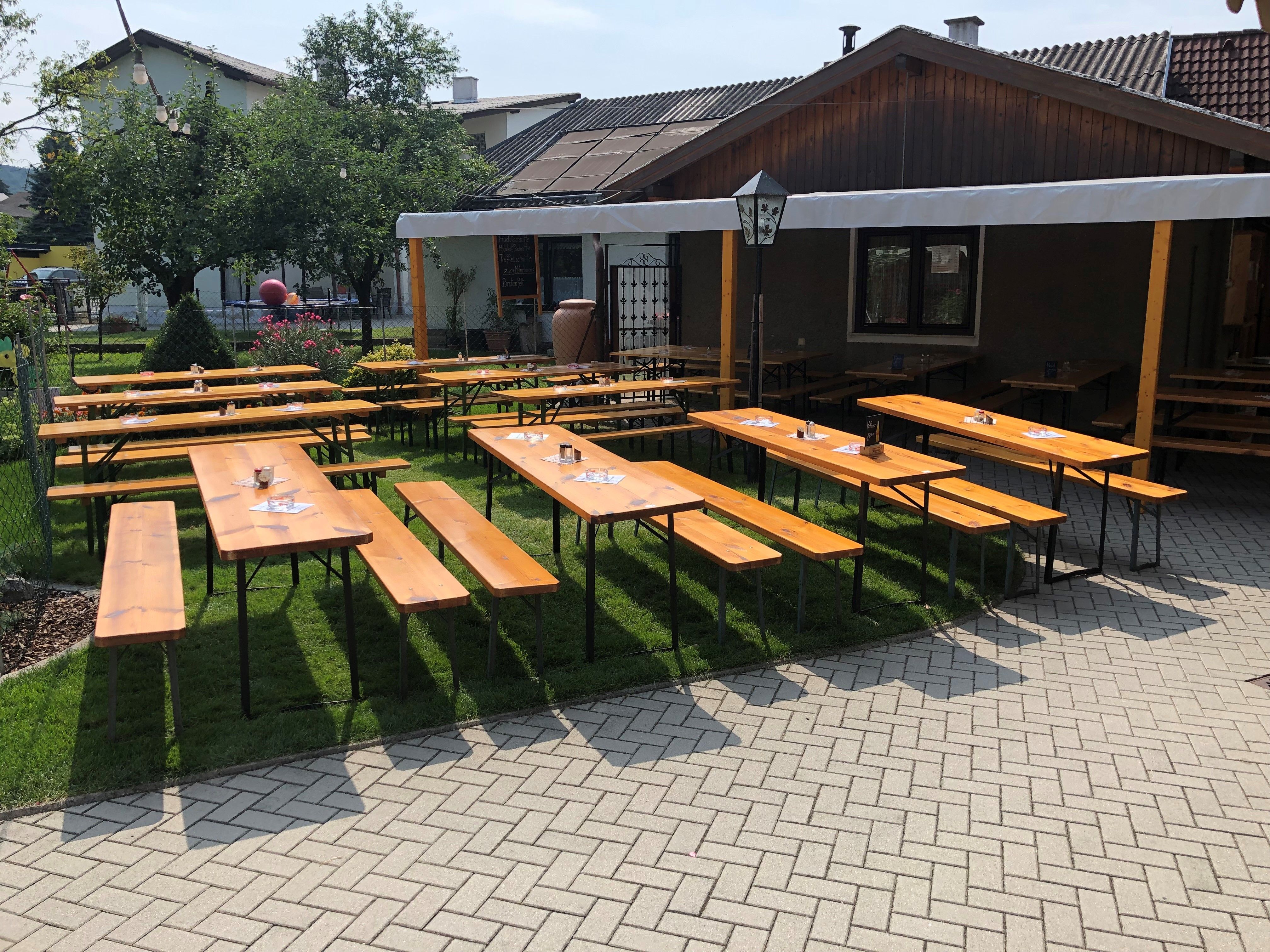 Dřevěné lavice a stoly v zahradě vinárny s ochranou proti slunci.