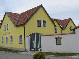 Žlutá budova s červenou střechou a zelenými vraty s nápisem "Guest House".