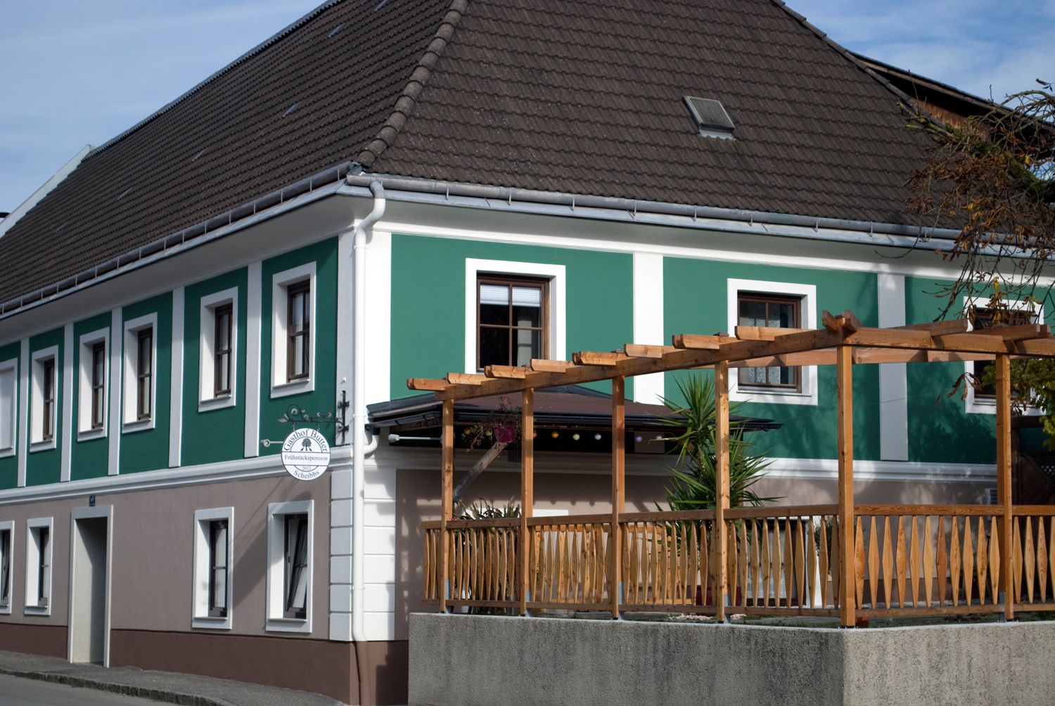 Exteriérový pohled na penzion se zelenobílou fasádou a dřevěnou pergolou.