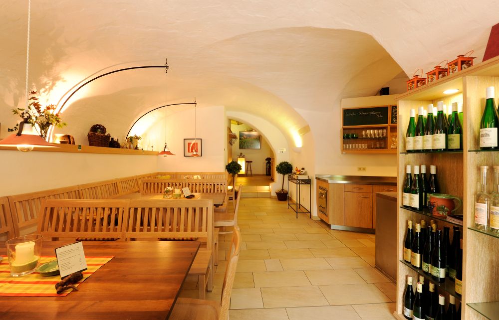 Pohled do interiéru útulné vinárny s dřevěnými stoly a stojany na víno.