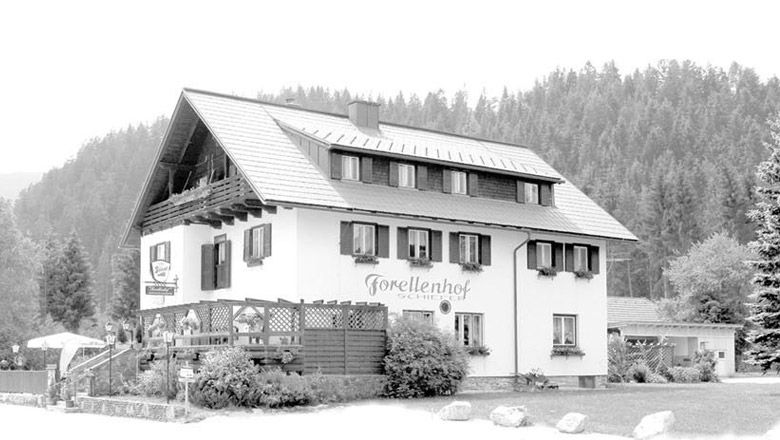 Tradiční hostinec s nápisem "Forellenhof Schiefer" na pozadí lesa.