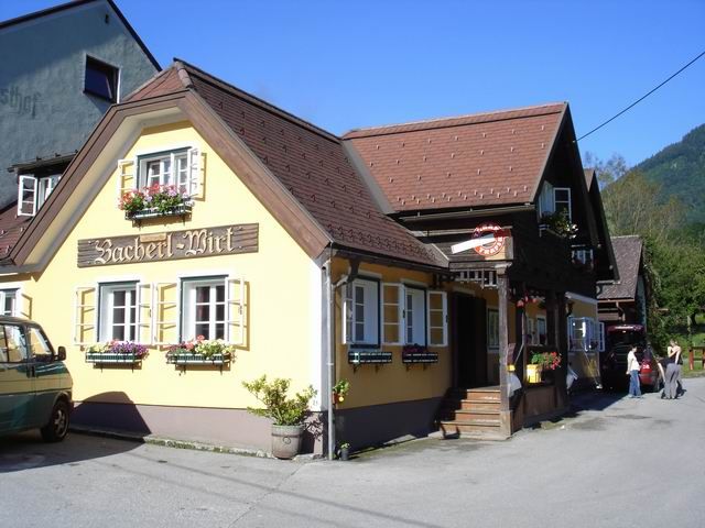 Tradiční hostinec se žlutou fasádou a květinovými truhlíky pod okny.