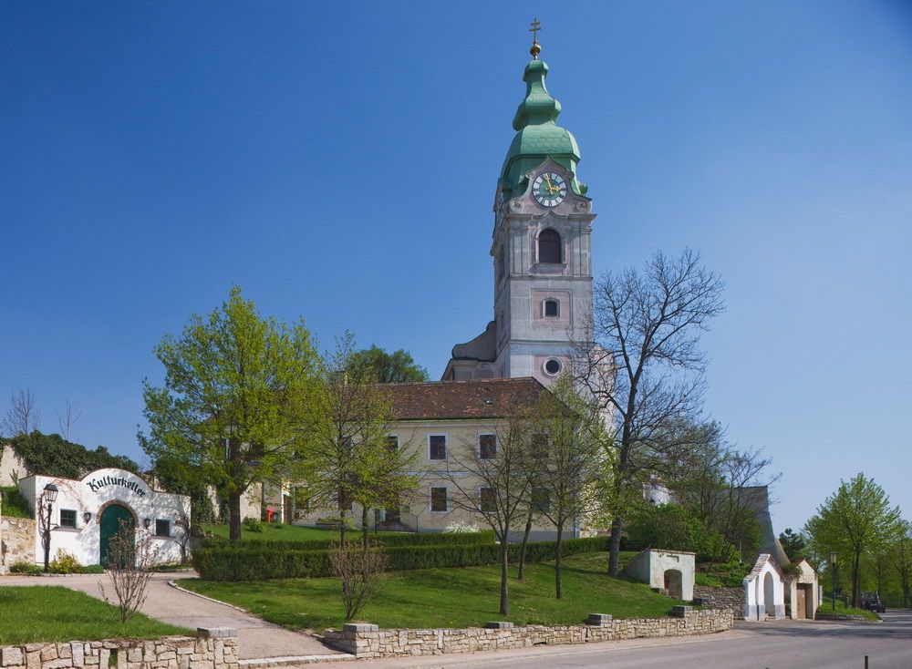 Kostel v Unterretzbachu se zelenou věží a okolními budovami.