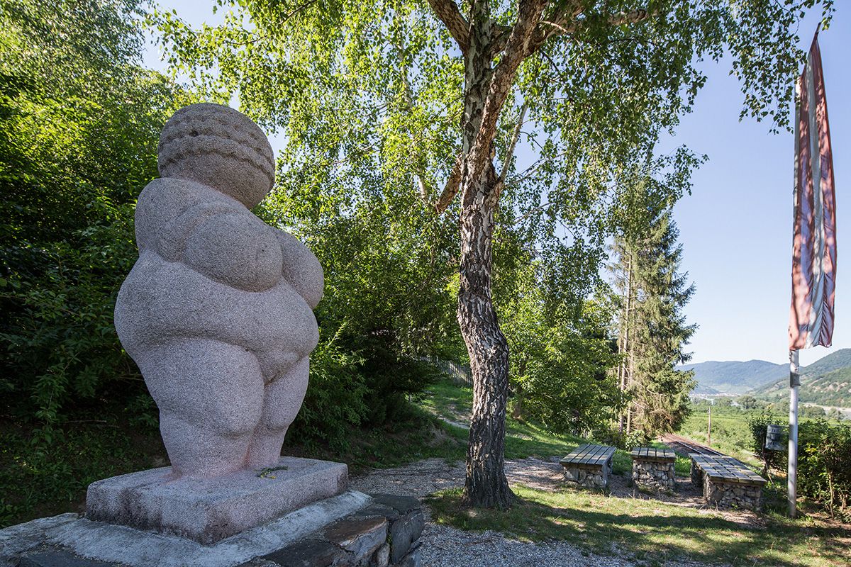 Venuše na podstavci v pozadí strom a lavičky