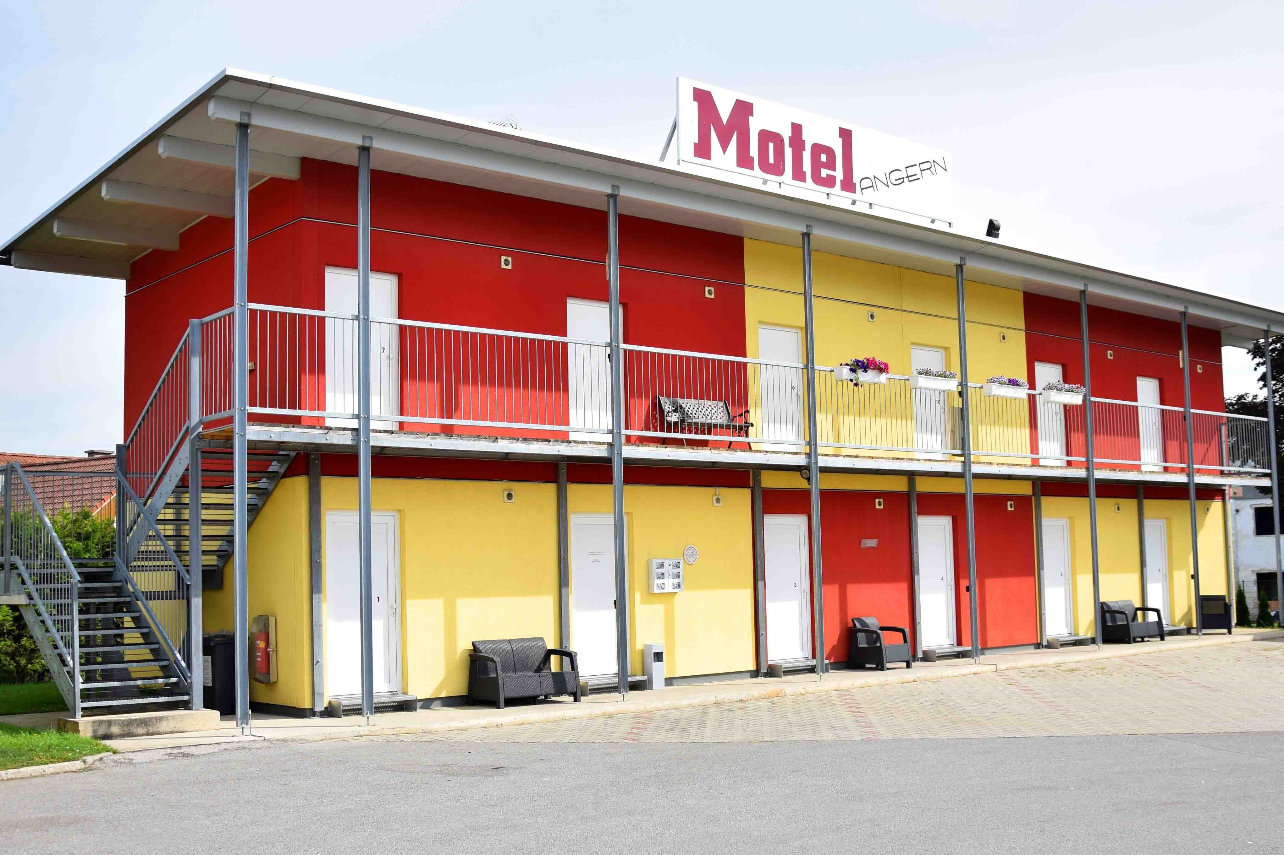 Dvoupatrová budova motelu se žlutými a červenými stěnami, schodištěm a balkonem.