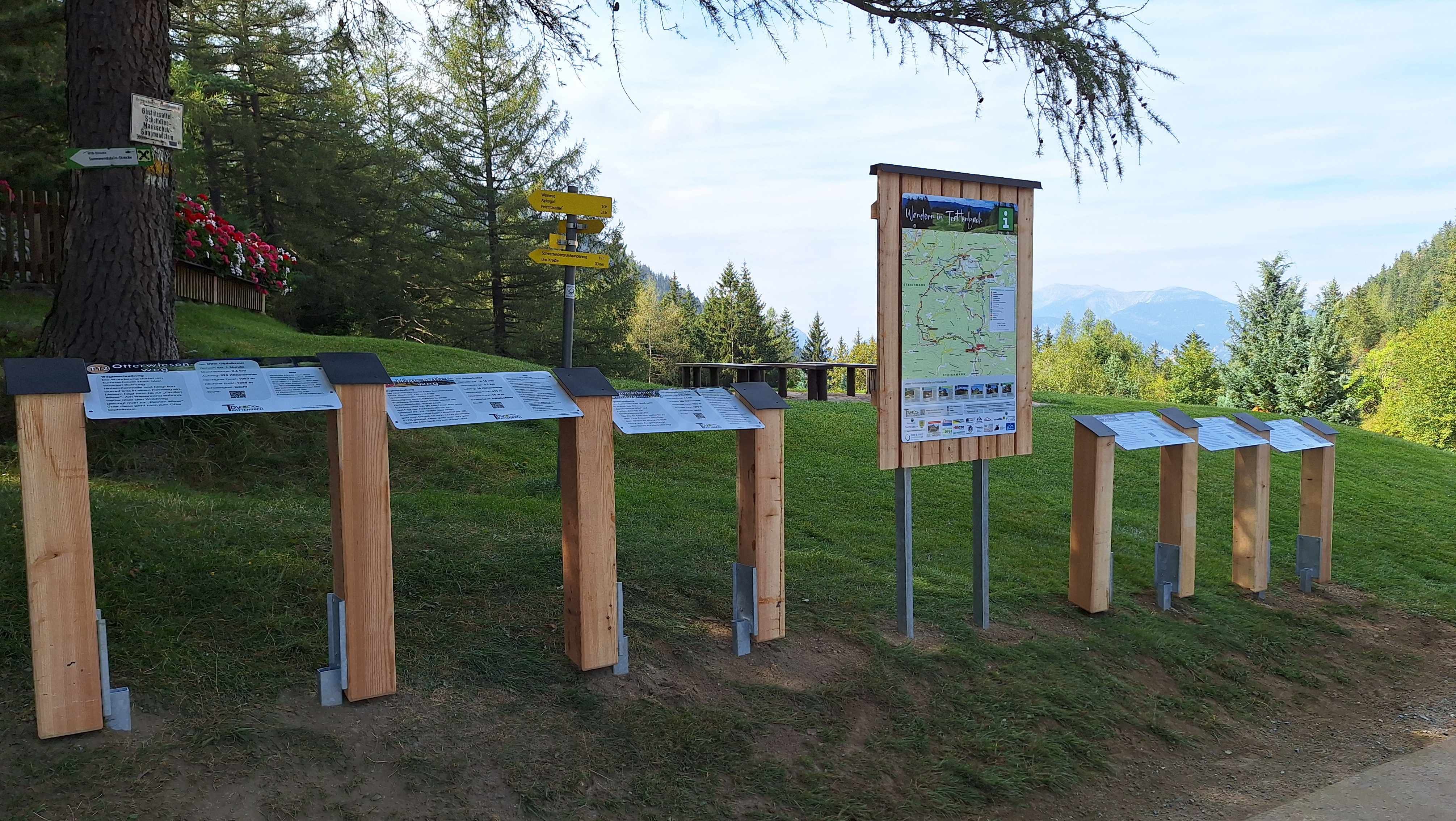 Turistické značení a informační tabule v zelené horské krajině.