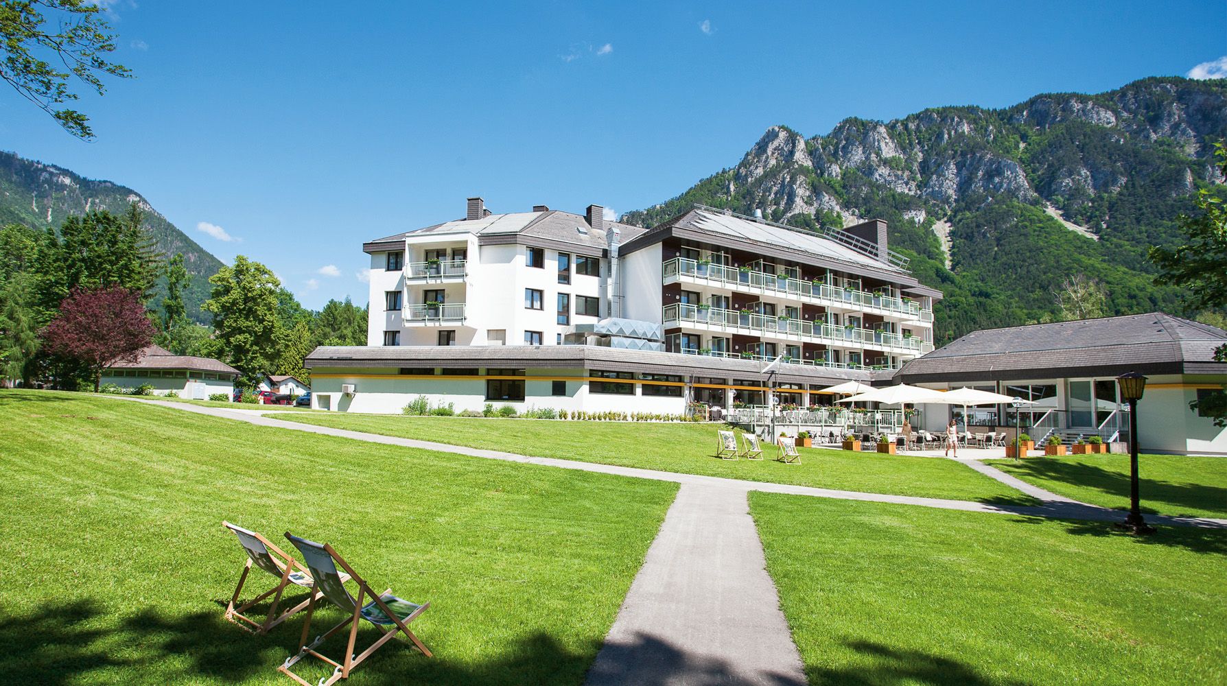 Parkhotel Hirschwang na pozadí hor se zeleným trávníkem a lehátky.