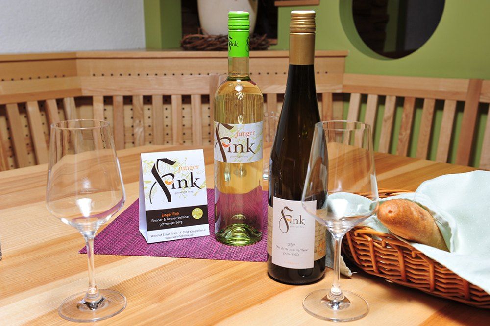 Dvě láhve vína a skleničky na dřevěném stole s košíkem na chleba.