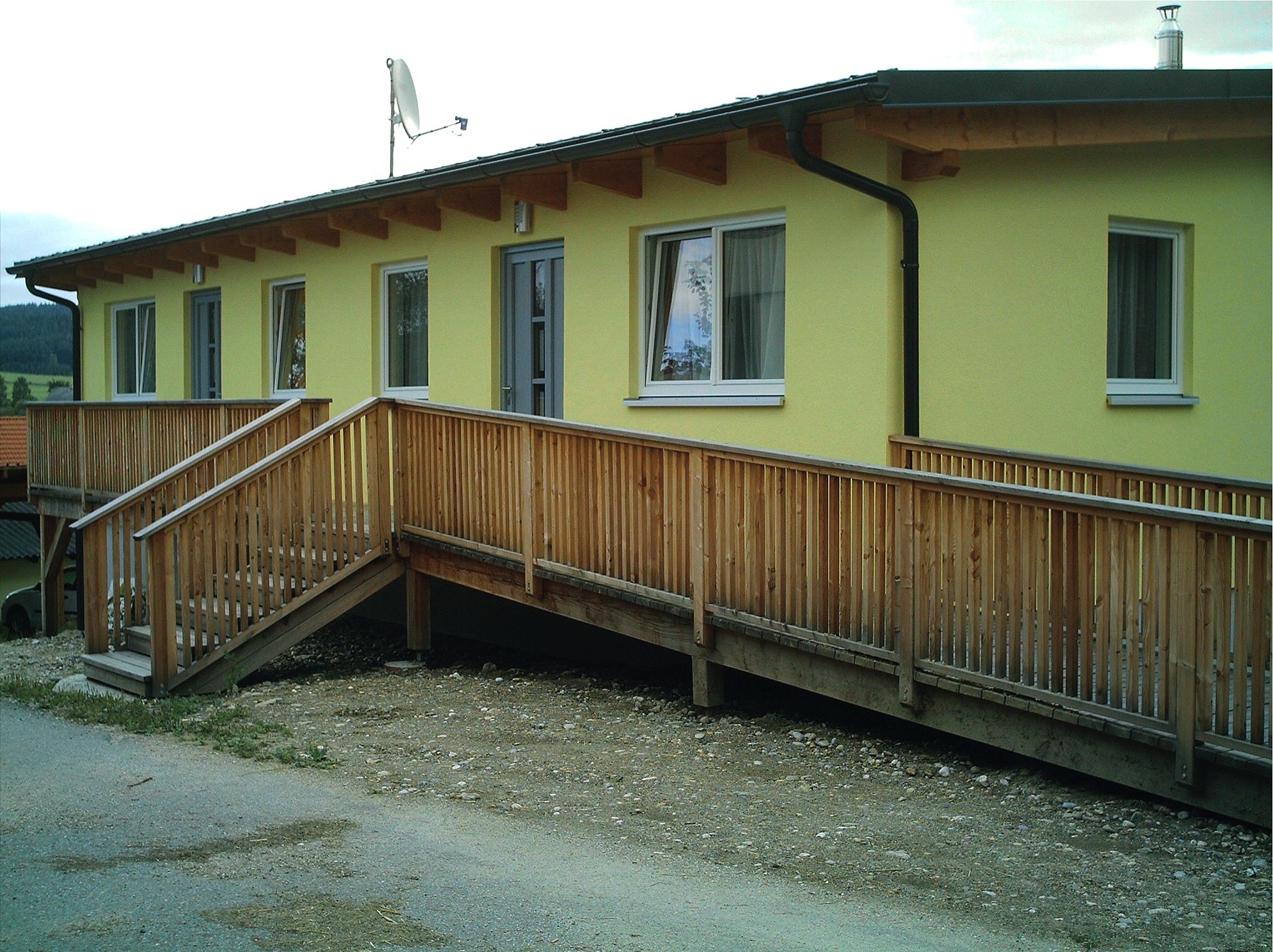 Žlutá budova s dřevěnou rampou a okny.
