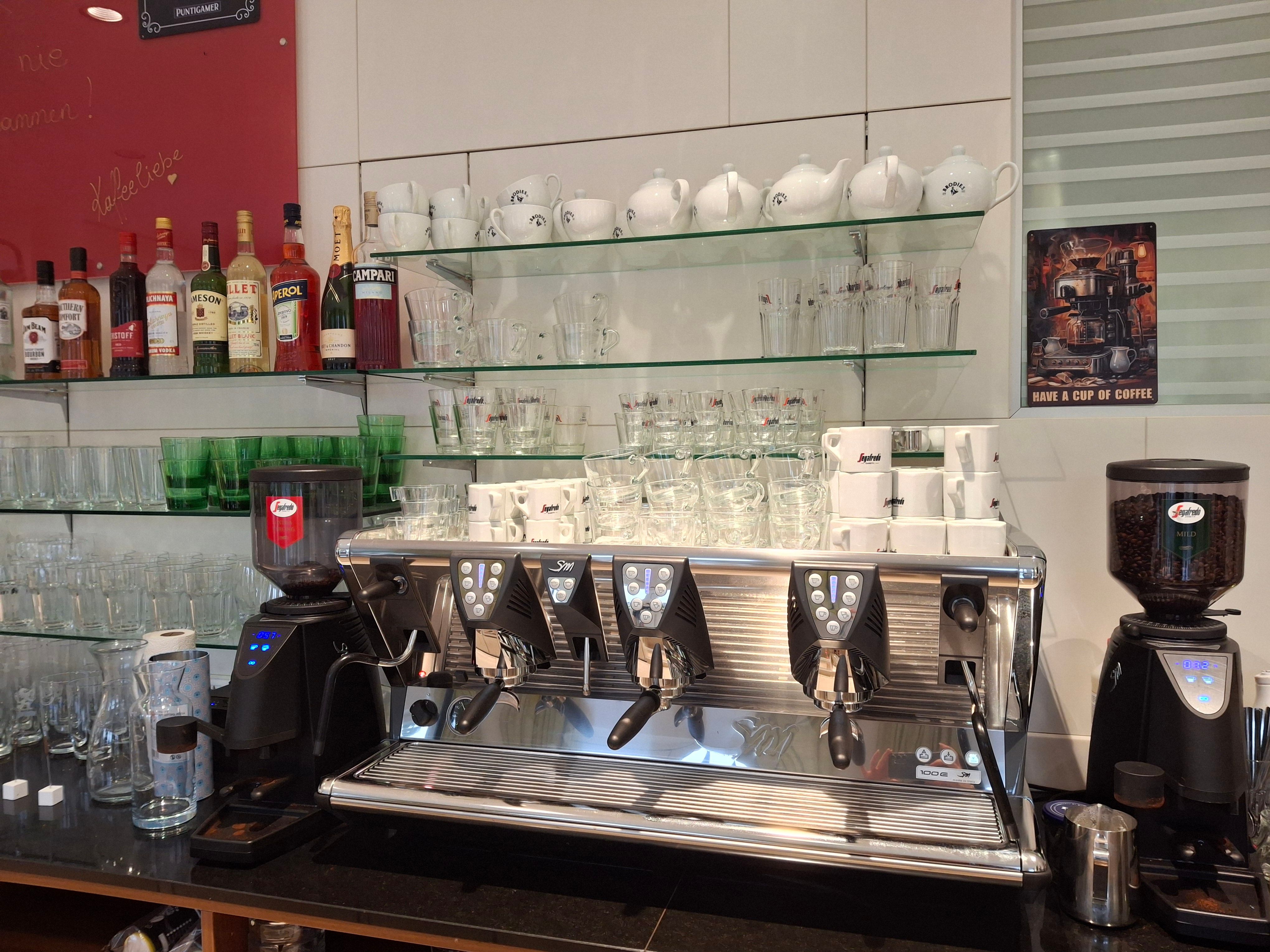 Kávovar s šálky a skleničkami v kavárně.