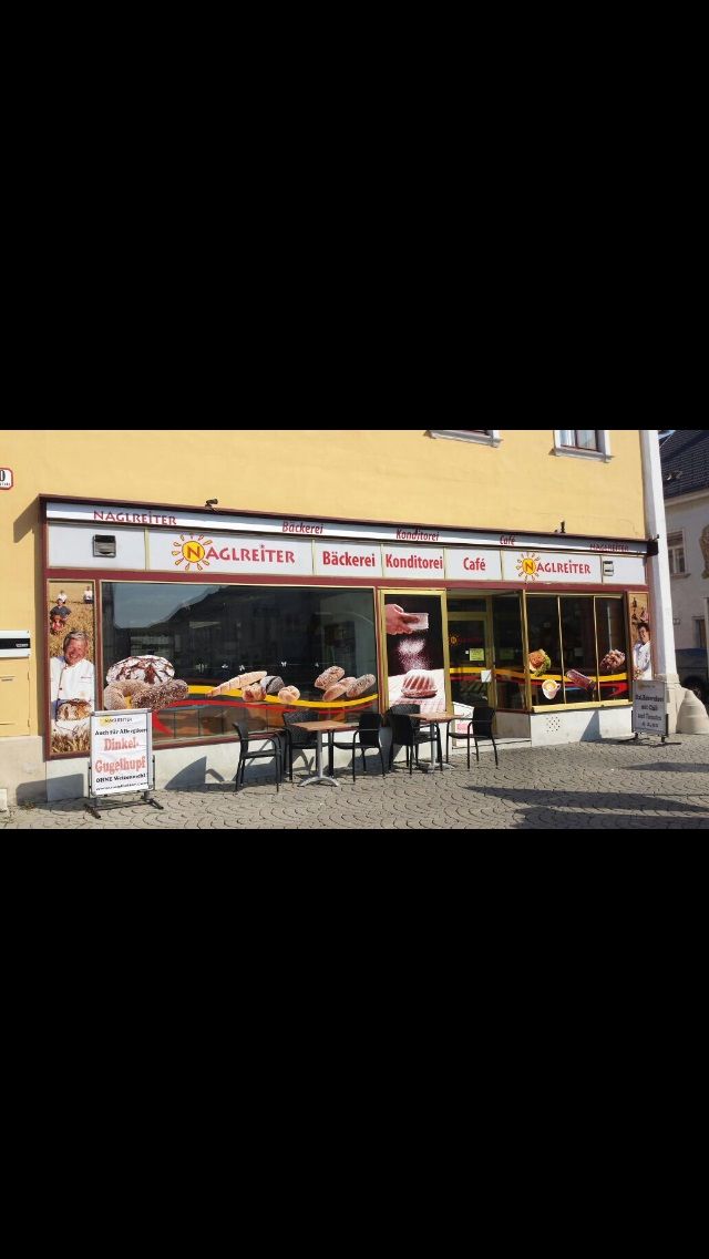Pohled zvenčí na Café-Bäckerei Naglreiter se stoly a židlemi před prodejnou.