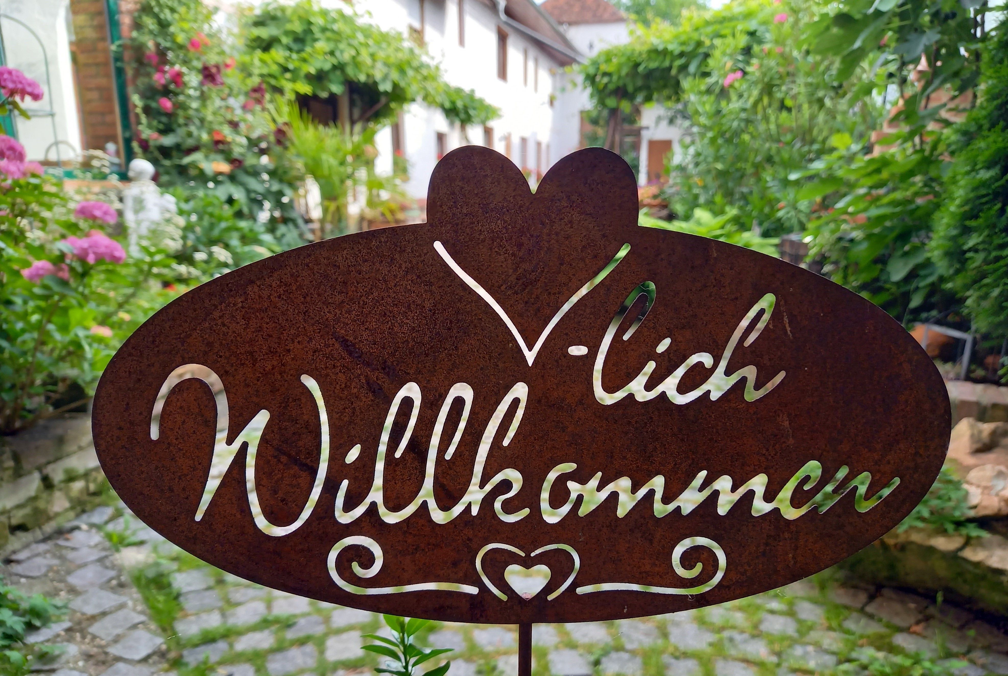 Kovová cedule s nápisem "Welcome" v zahradě.