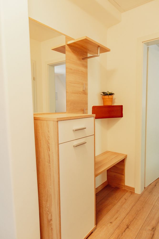 Moderní předsíň s dřevěnou skříní, zrcadlem a rostlinou.