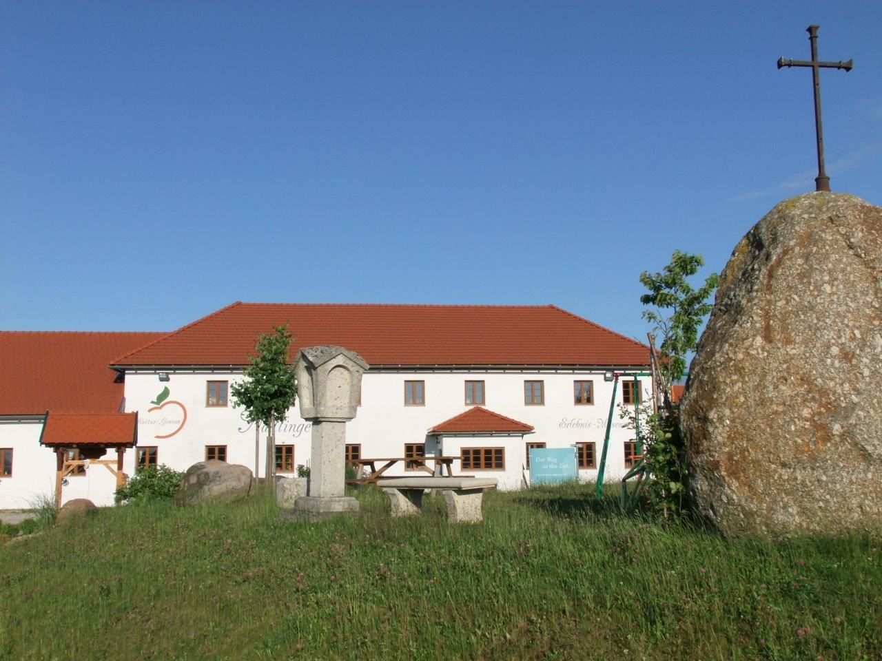Statek s červenou střechou a velkým kamenem s křížem v popředí.