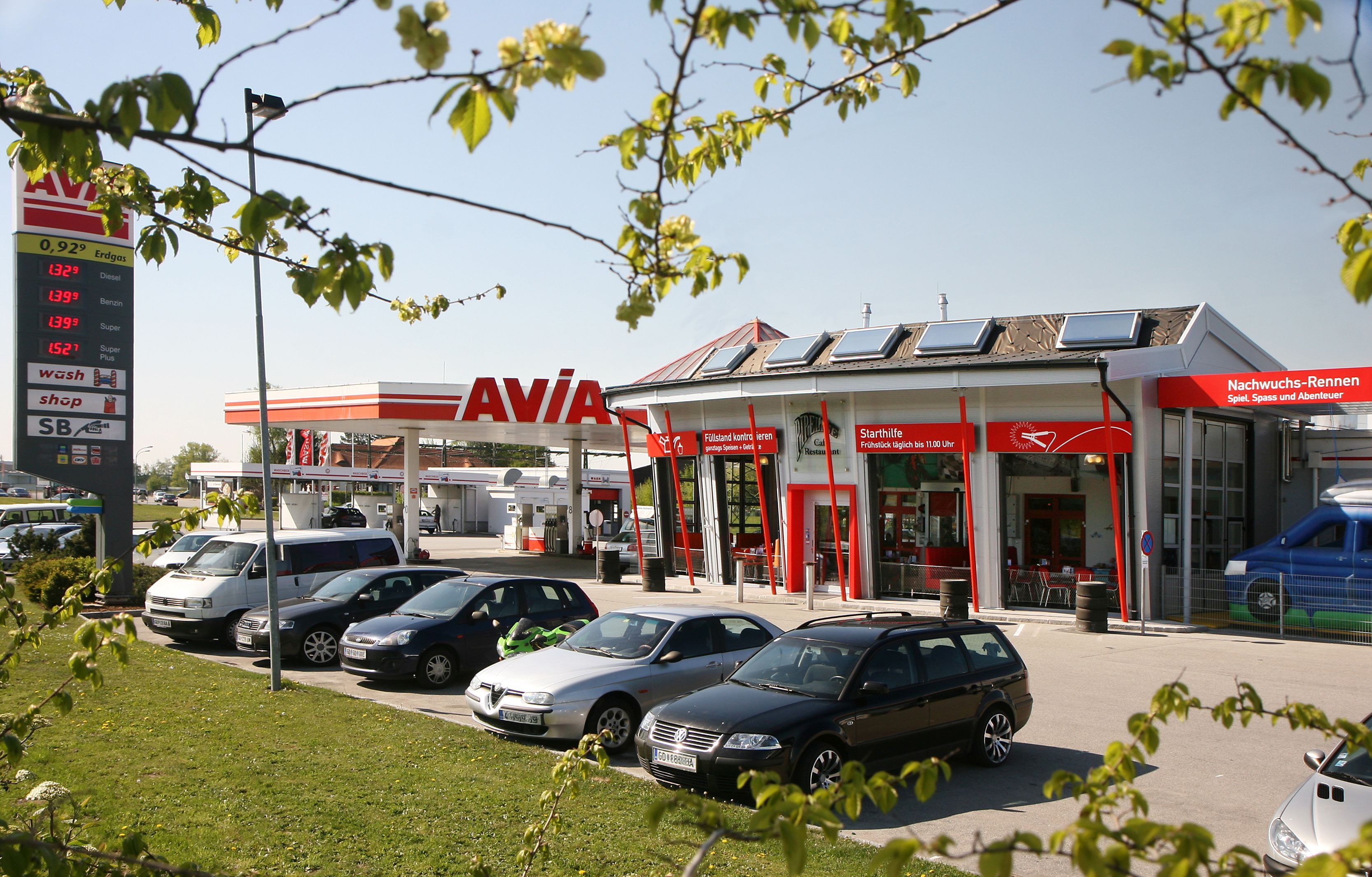 Čerpací stanice s logem AVIA a několika zaparkovanými auty v popředí.