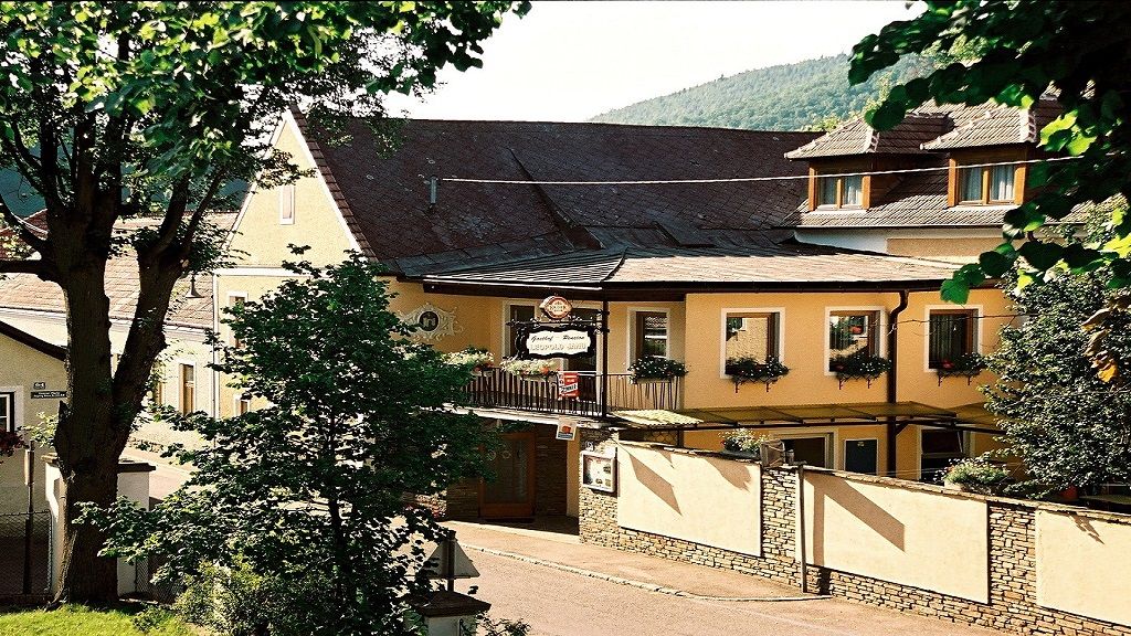 Exteriérový pohled na penzion Leopold Janu se žlutou fasádou a květinovými truhlíky.