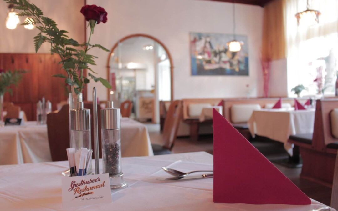Pohled do interiéru útulné restaurace s prostřenými stoly, červenými ubrousky a růží ve váze.
