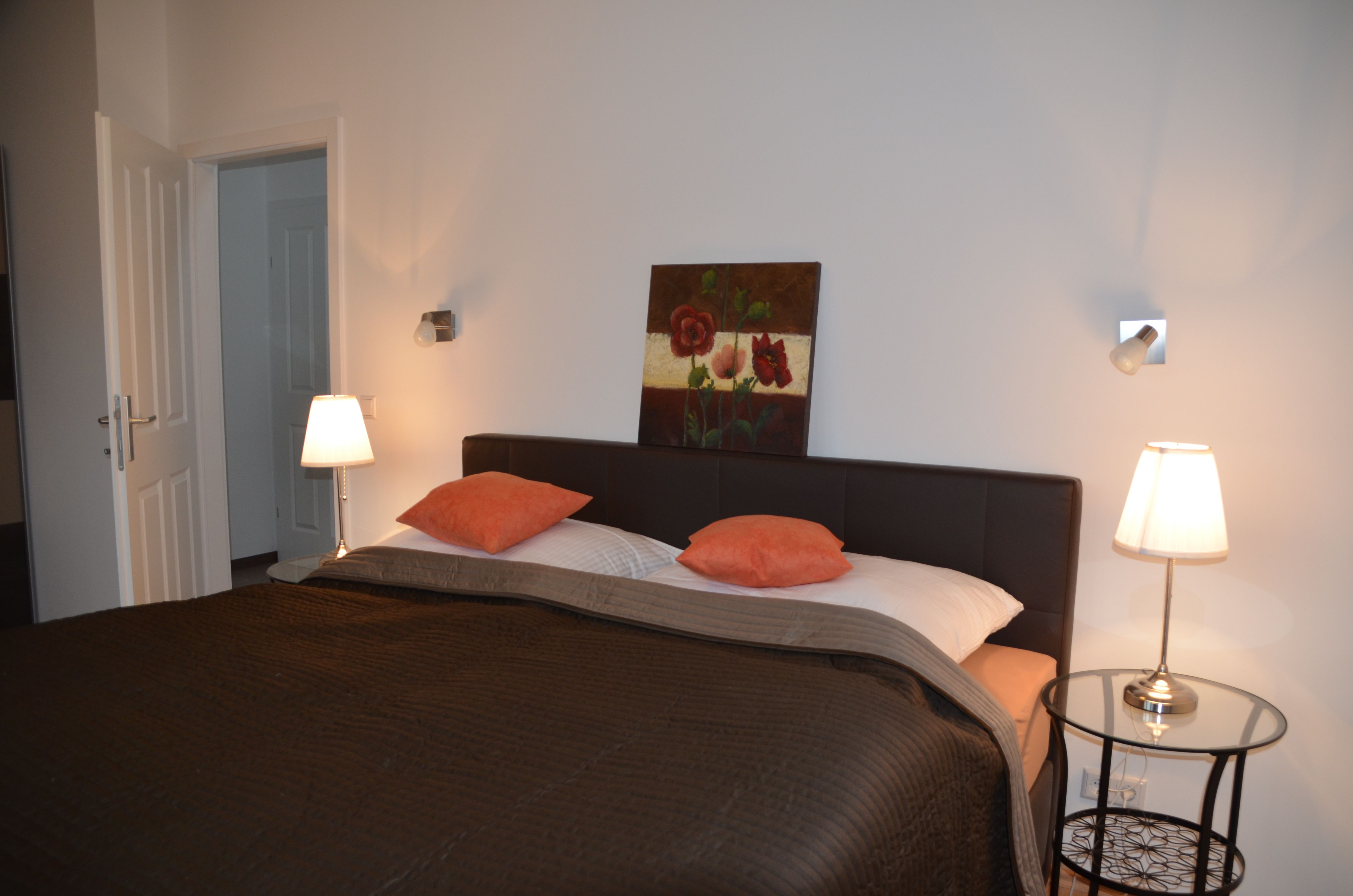 Ložnice s manželskou postelí, dvěma nočními lampičkami a obrazem na stěně.