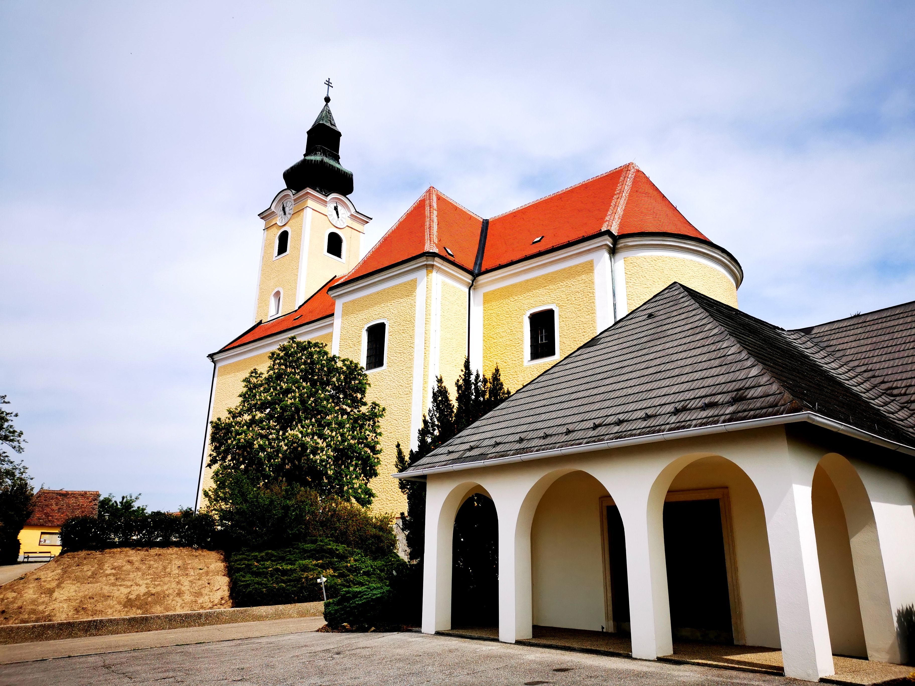 Farní kostel svatého Mikuláše v Röschitzu se žlutou fasádou a červenou střechou.