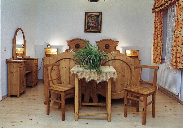 Rustikální ložnice s dřevěným nábytkem, manželskou postelí, stolem s rostlinou a zrcadlem.
