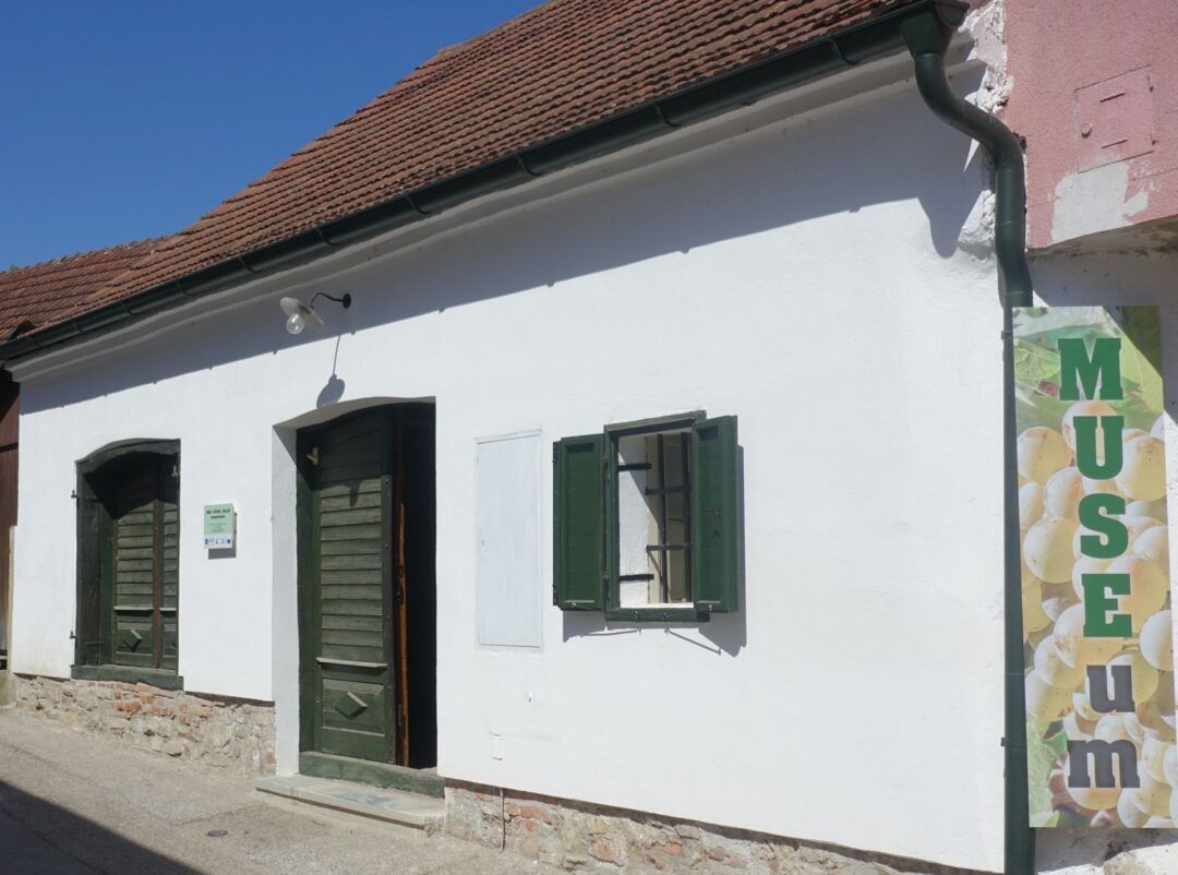 Bílá budova se zelenými okenicemi a dveřmi, nápis "MUSEUM".