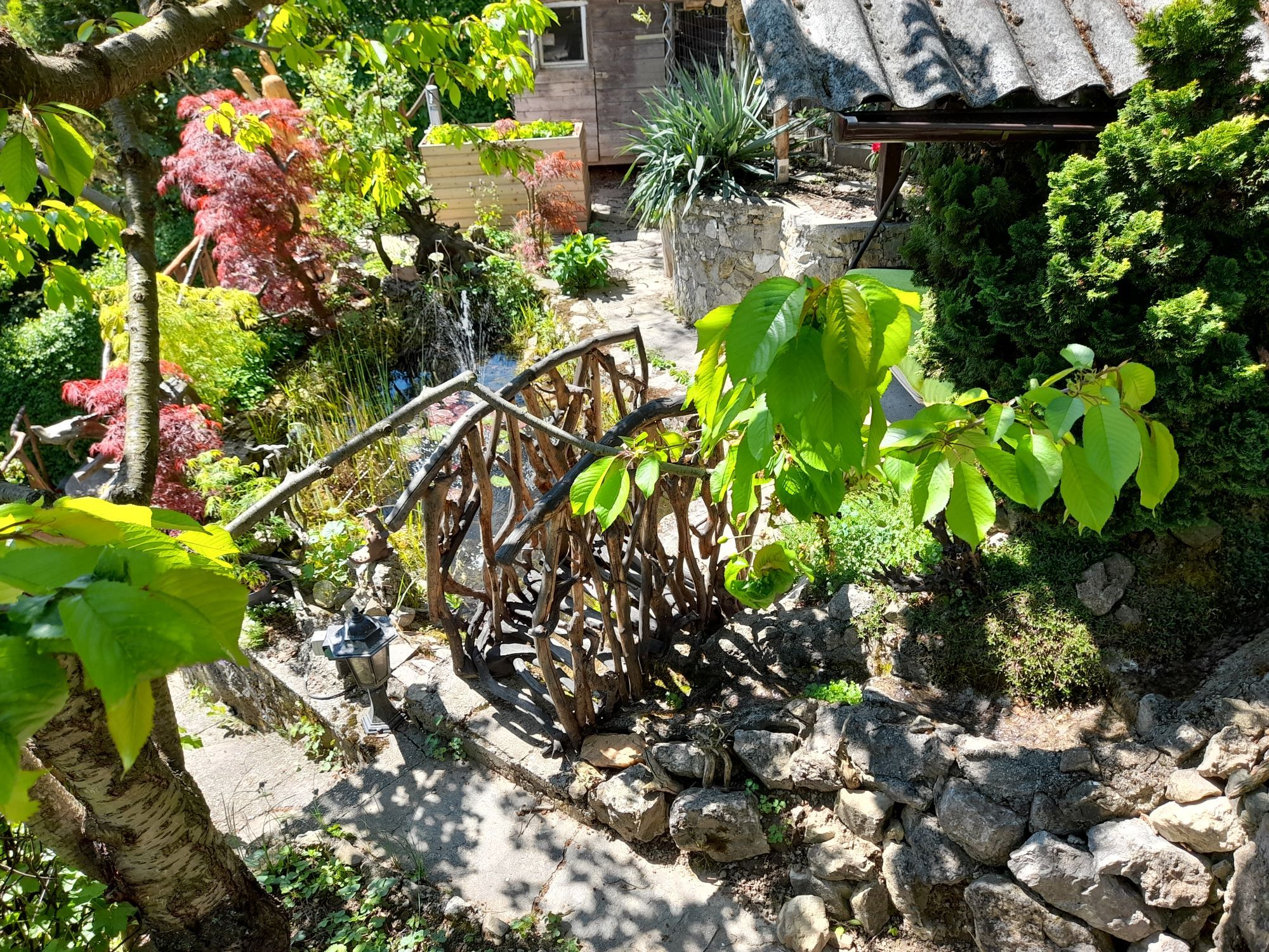 Zahrada s dřevěným mostem, rostlinami a kameny.