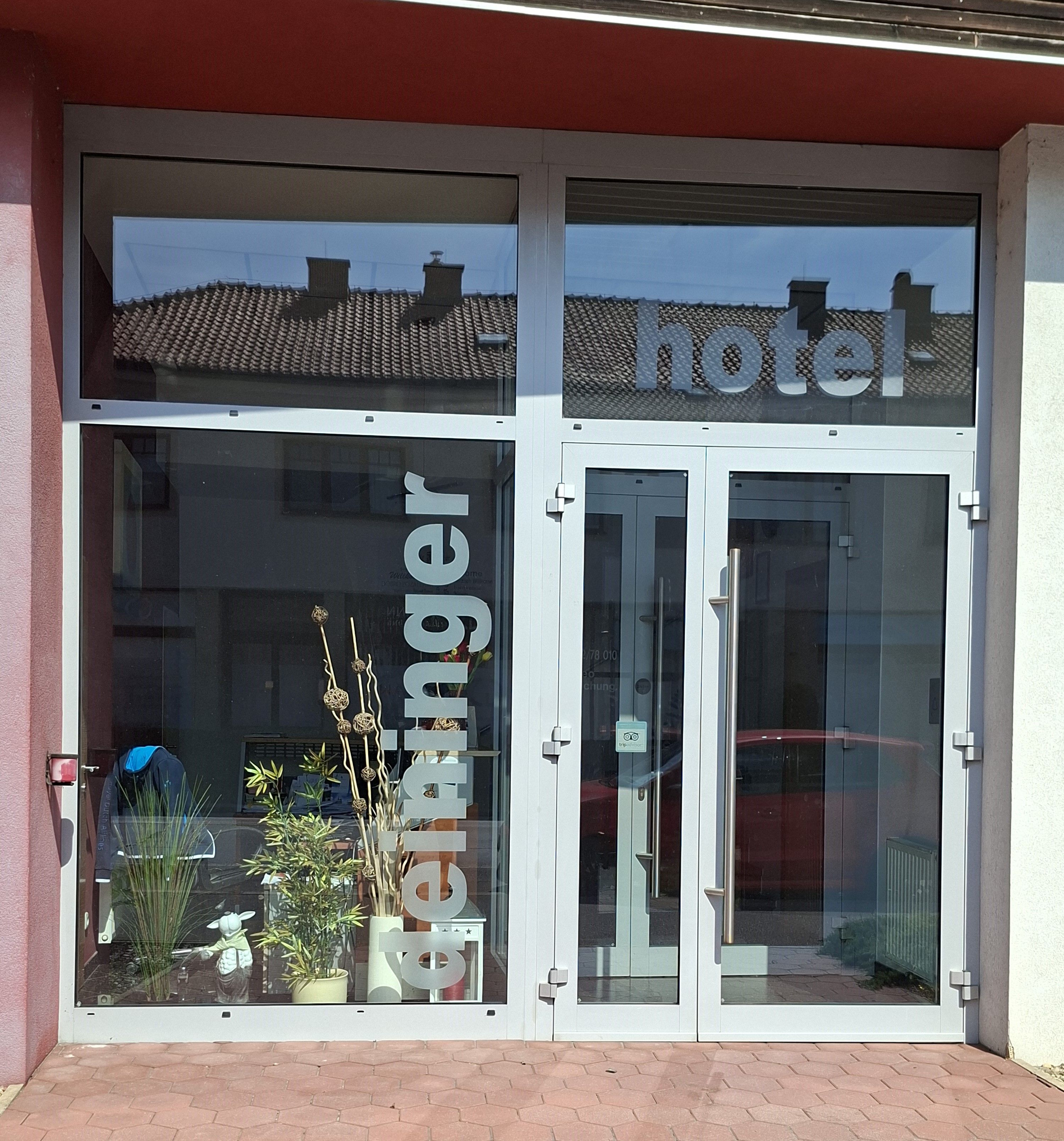 Vchod do hotelu Deininger s proskleným průčelím a rostlinami.