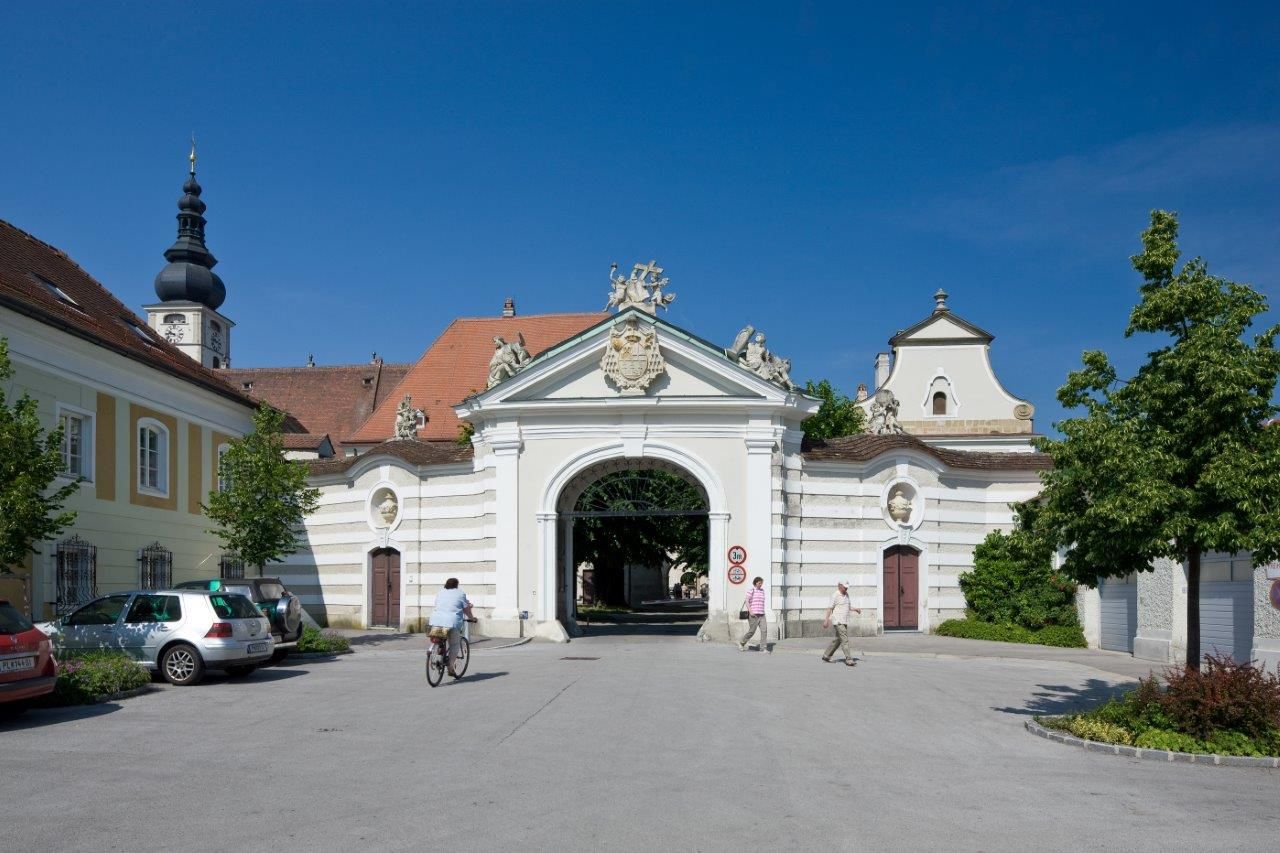 Historická budova diecéze s podloubím a kostelní věží v pozadí.